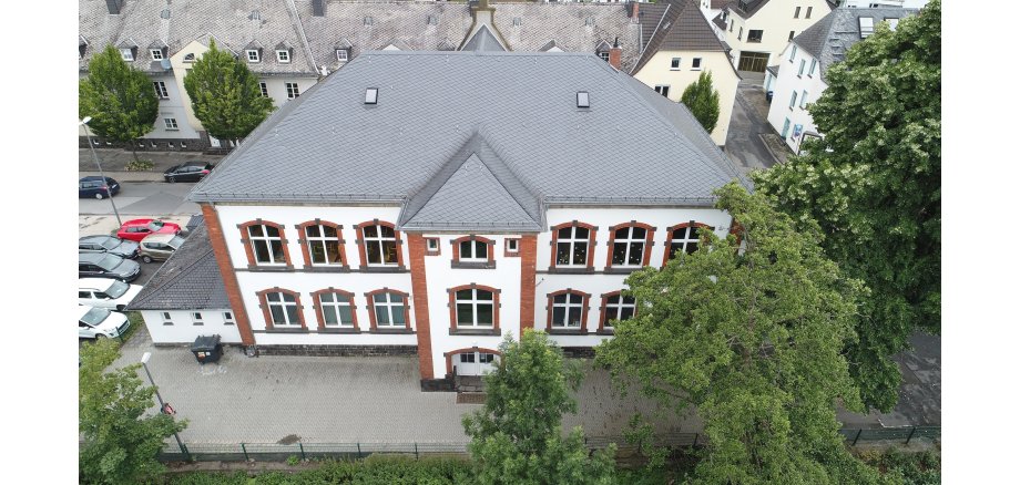Luftaufnahme Grundschule Clemens, graues Dach und Fassade hell mit roten Fenster und Tür Umrandungen