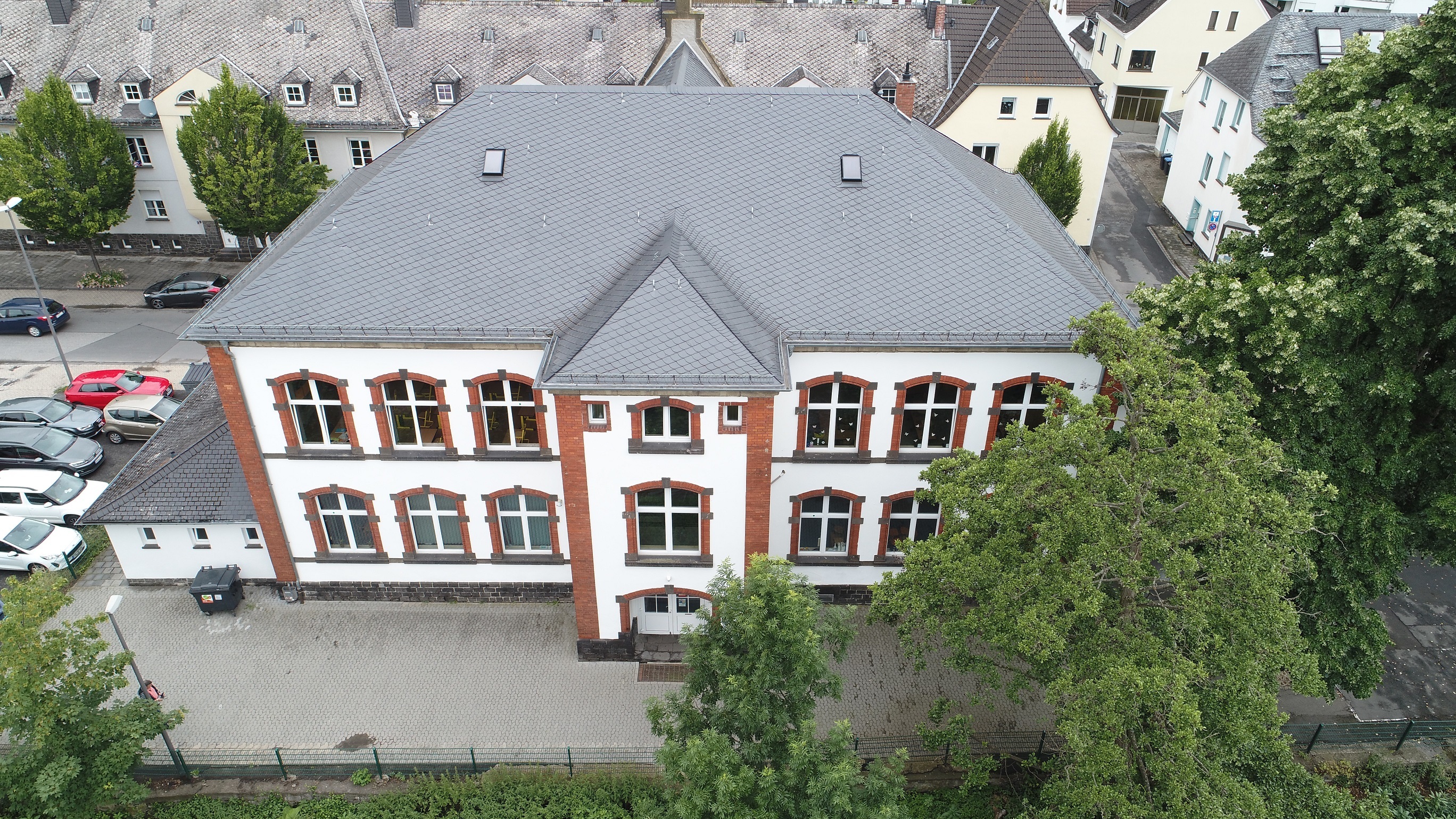 Luftaufnahme Grundschule Clemens, graues Dach und Fassade hell mit roten Fenster und Tür Umrandungen