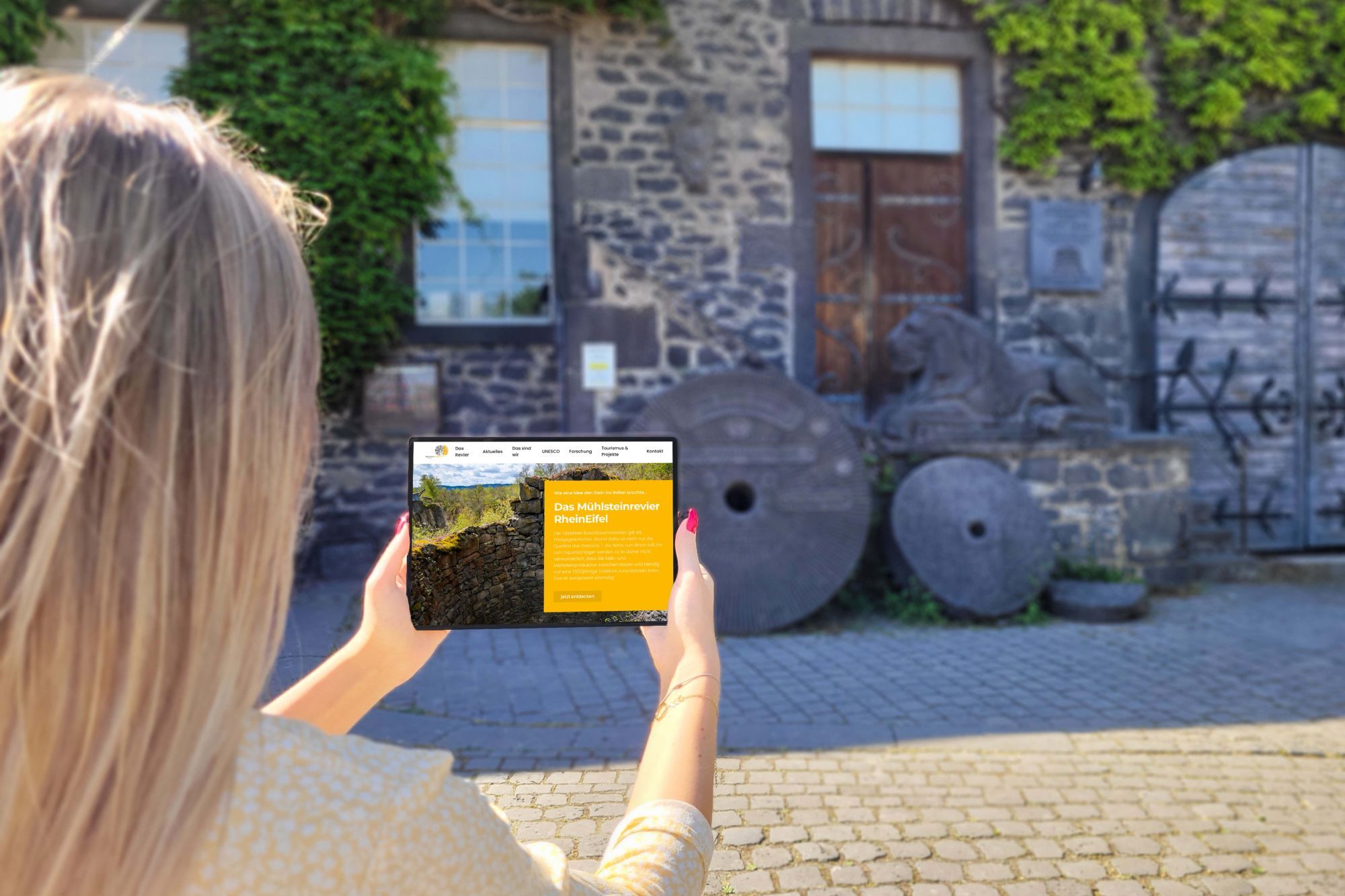Frau mit IPad in der Hand. Die Seite des Mühlsteinreviers ist geöffnet