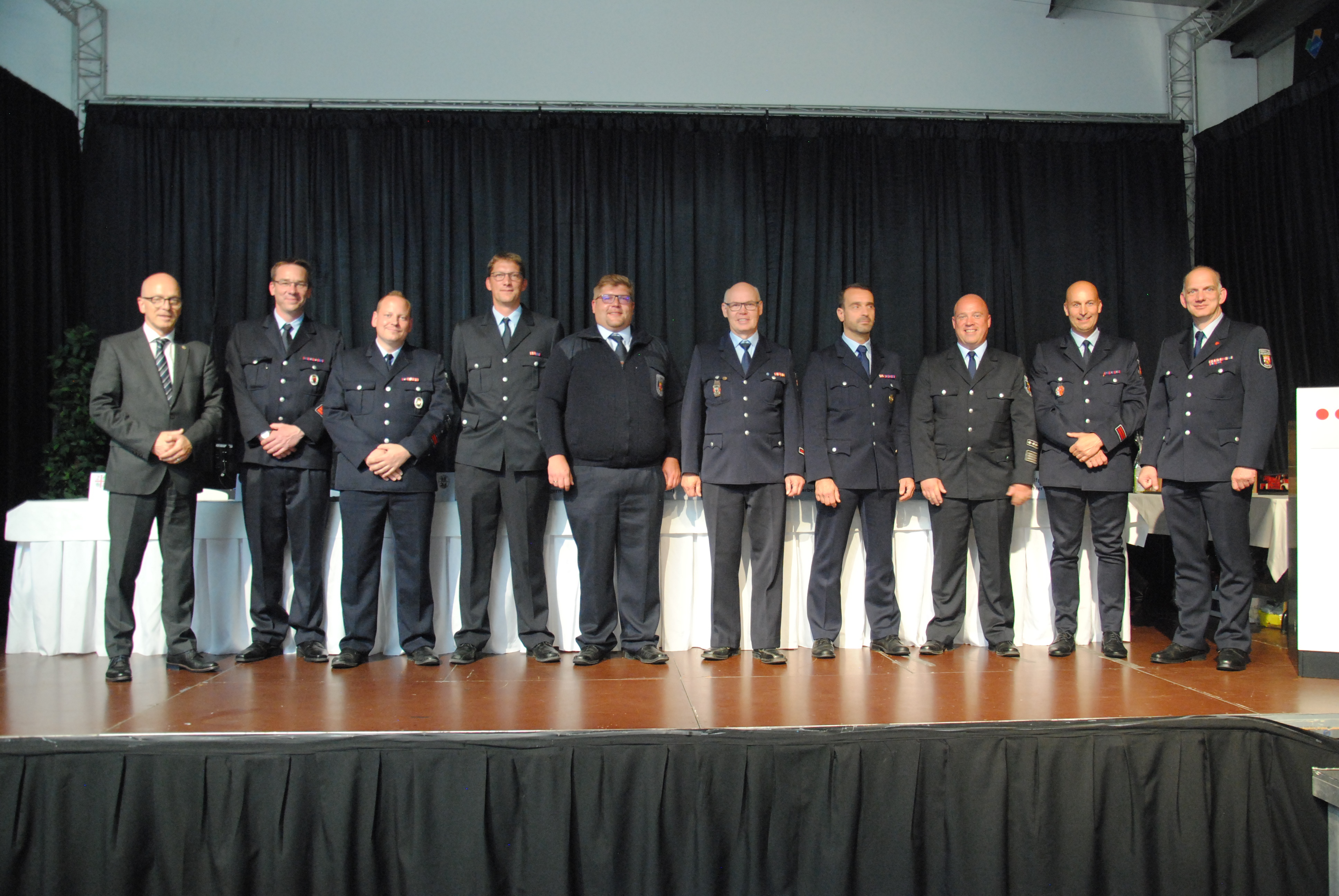 10 Personen in Ausgehuniform auf einer Bühne