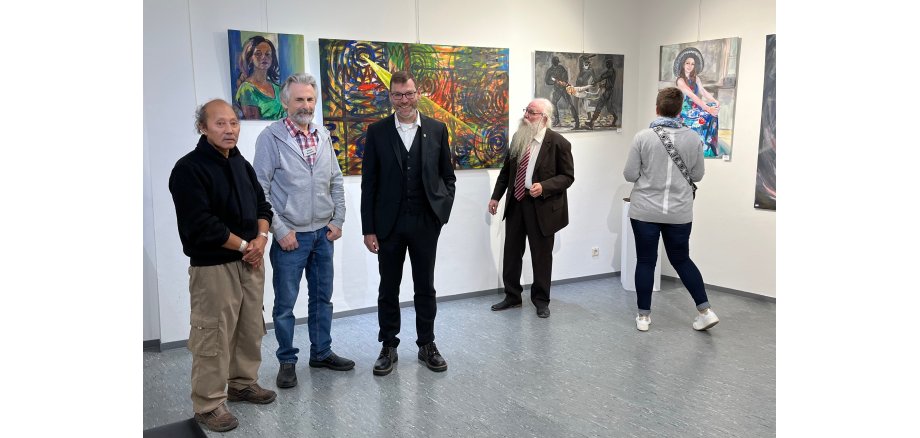 Mehrere Personen stehen in der Ausstellung nebeneinander im Hintergrund Bilder der Kunstausstellung
