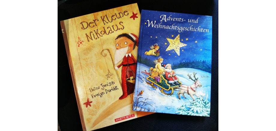 orangenes Buch mit dem roten Titel - der Kleine Nikolaus darüber schräg liegend ein Blaues Buch mit dem Titel Advents- und Weihnachtsgeschichten in weißer Schrift , Grafik Weihnachtsmann auf Schlitten an Rentier