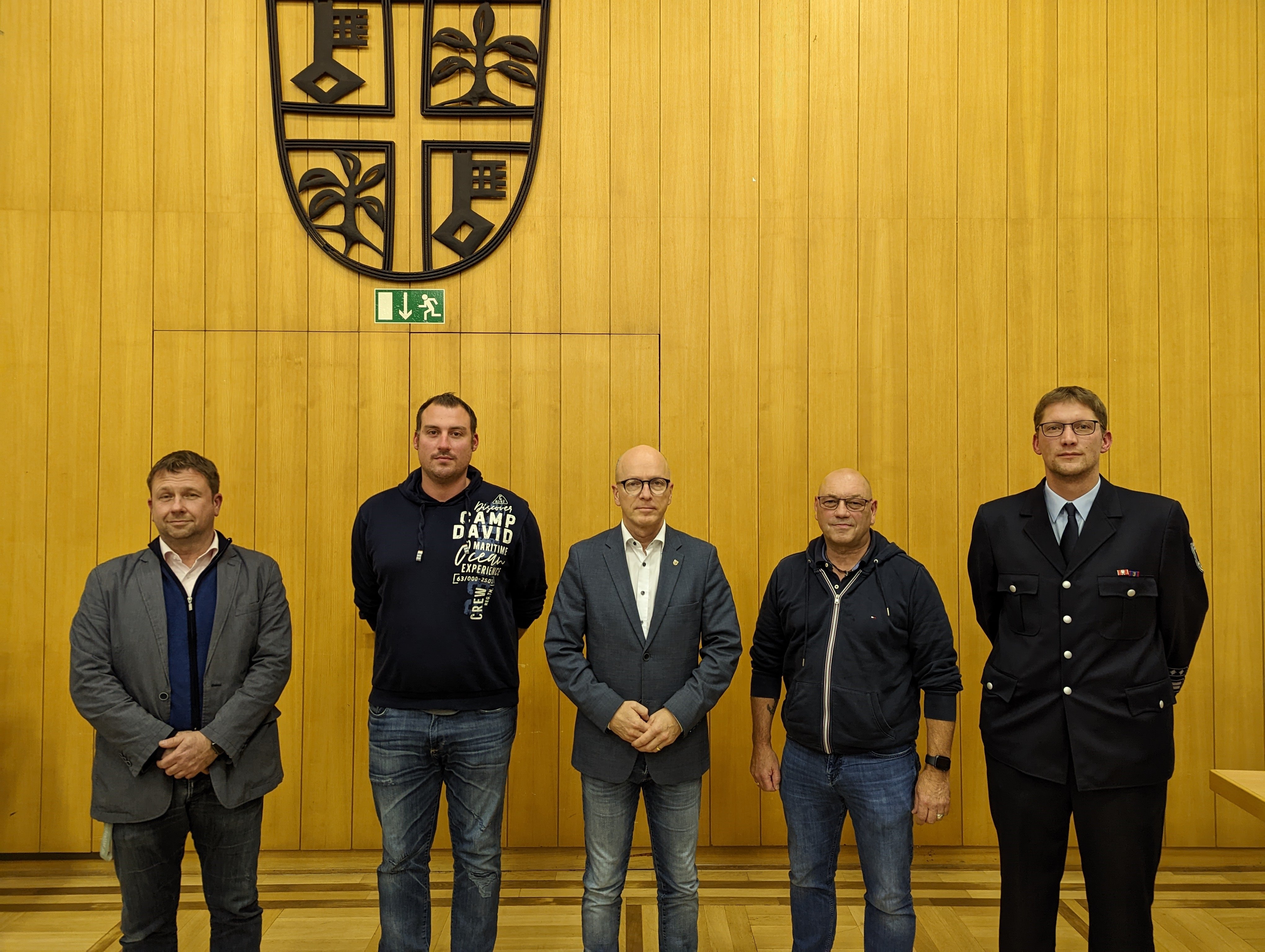 Fünf Männer stehen vor einer Holzwand