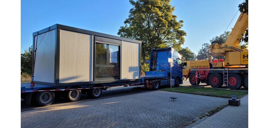 LKW mit einem Container auf der Ladefläche, daneben ein Kran