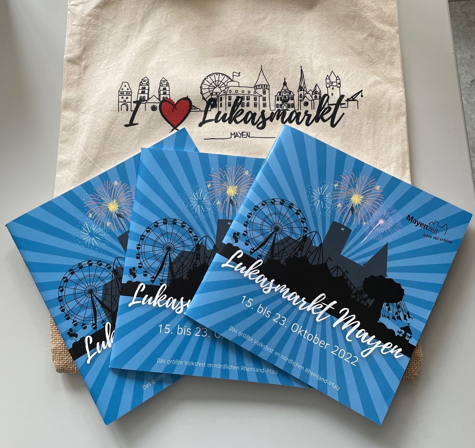 Drei Hefte auf einer Tasche mit dem Lukasmarktlogo