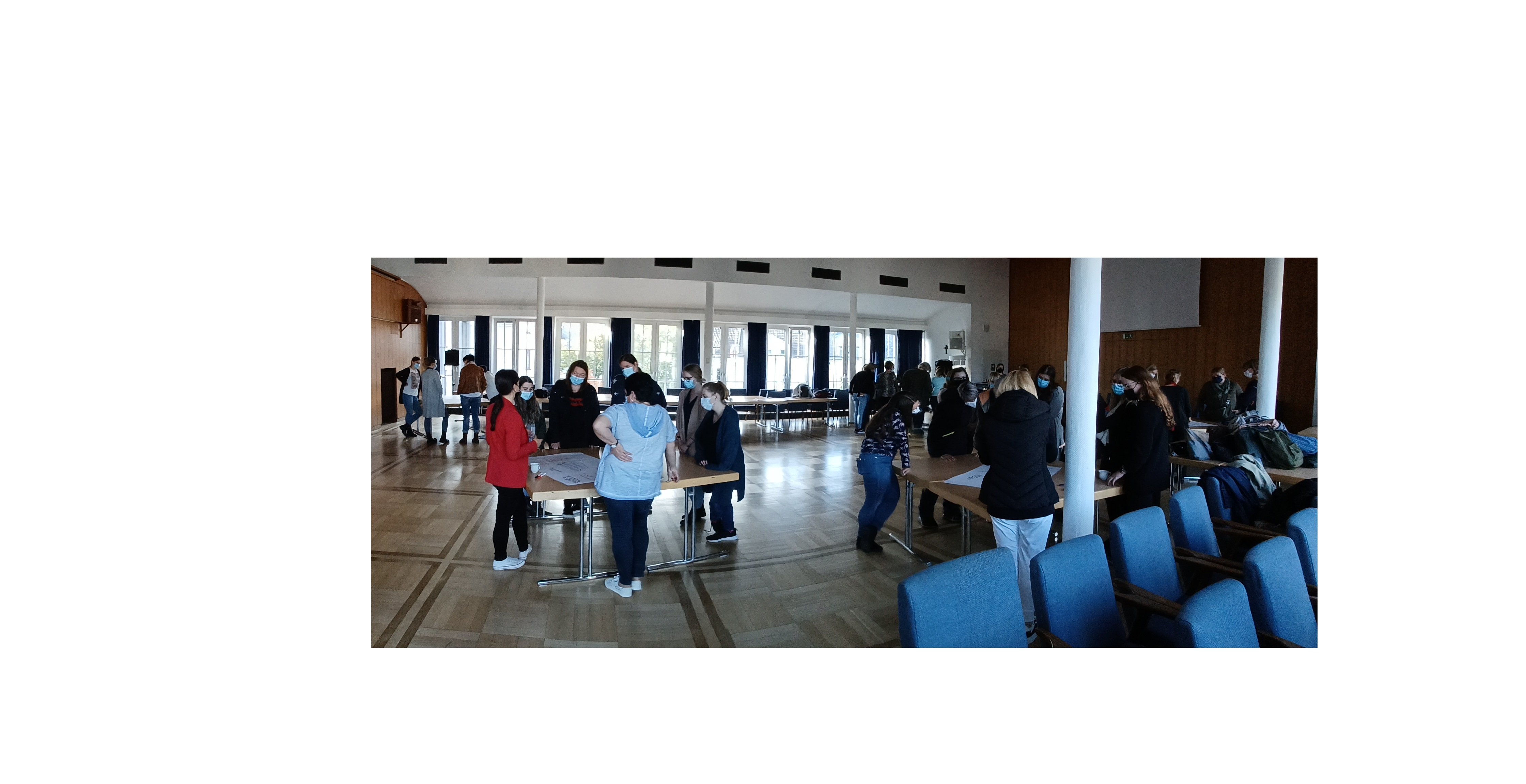 Zahlreiche Frauen stehen in kleinen Gruppen an verschiedenen Tischen und unterhalten sich.