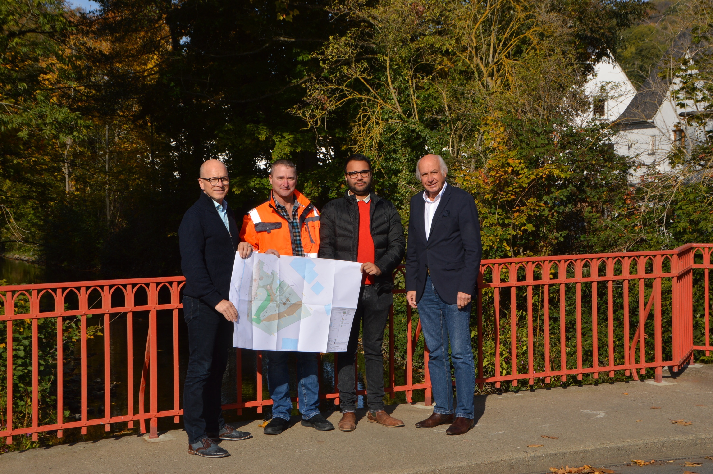 Vier Personen auf einer Brücke mit rotem Geländer - einer hält einen Plan in der Hand