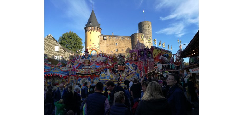 Viele Menschen stehen vor Fahrgeschäft an Lukasmarkt und die Burg ist im Hintergrund