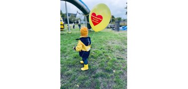 Kind mit Luftballon auf der Wiese vor einer Rutsche