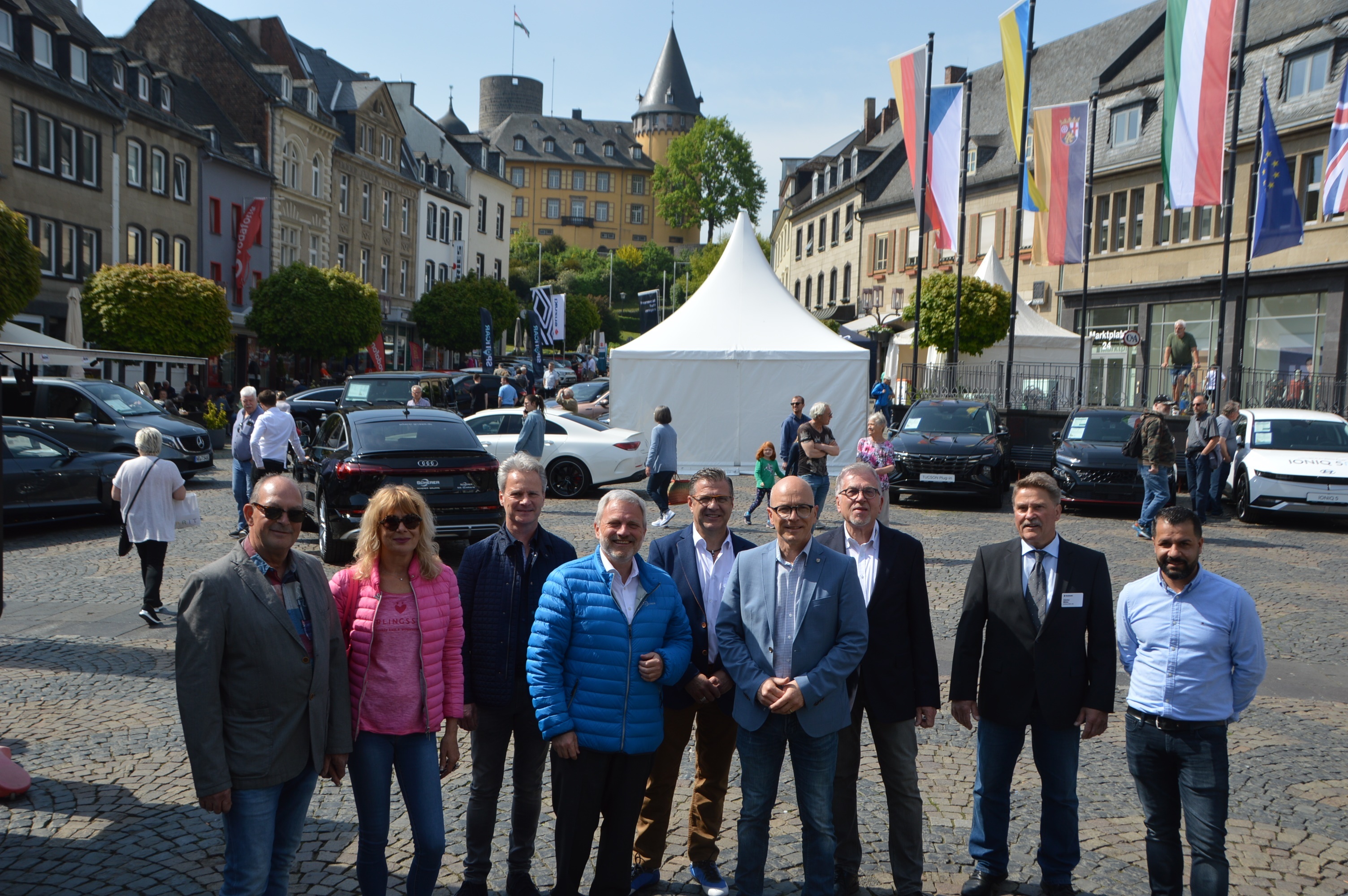 Eine Gruppe von Personen steht auf dem Marktplatz für ein Bild zusammen - im Hintergrund sind Autos zu sehen