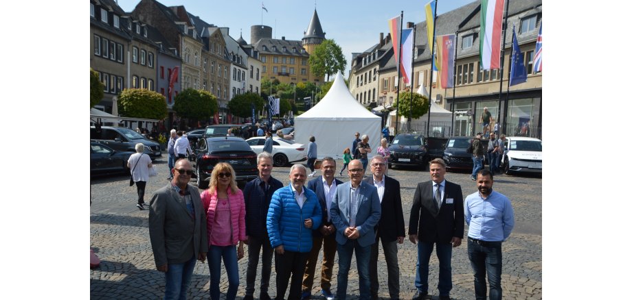 Eine Gruppe von Personen steht auf dem Marktplatz für ein Bild zusammen - im Hintergrund sind Autos zu sehen