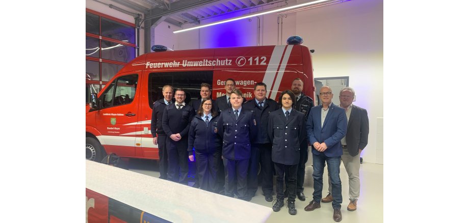 Eine Gruppe von Menschen steht vor einem Feuerwehrauto in einer Halle