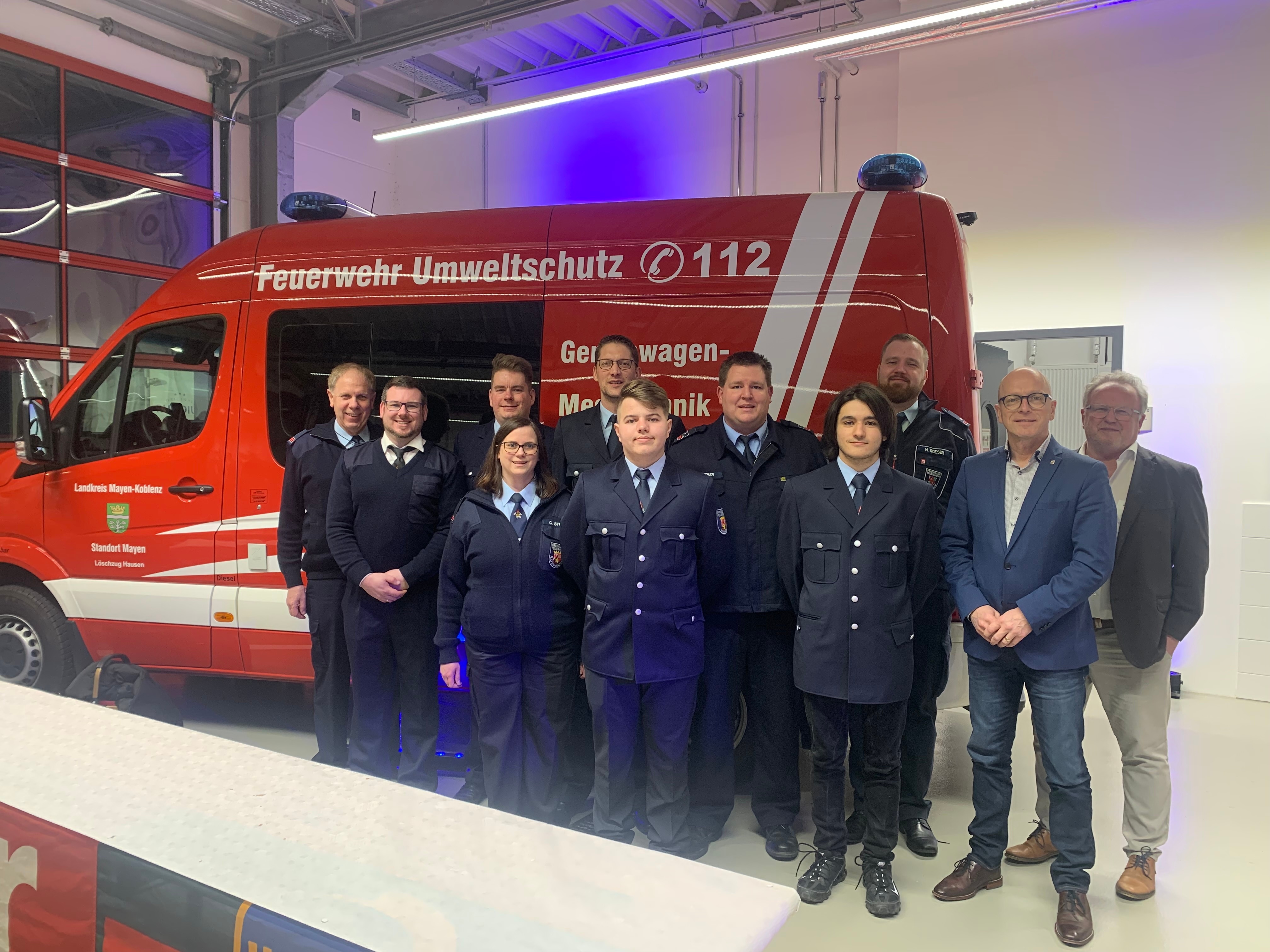 Eine Gruppe von Menschen steht vor einem Feuerwehrauto in einer Halle