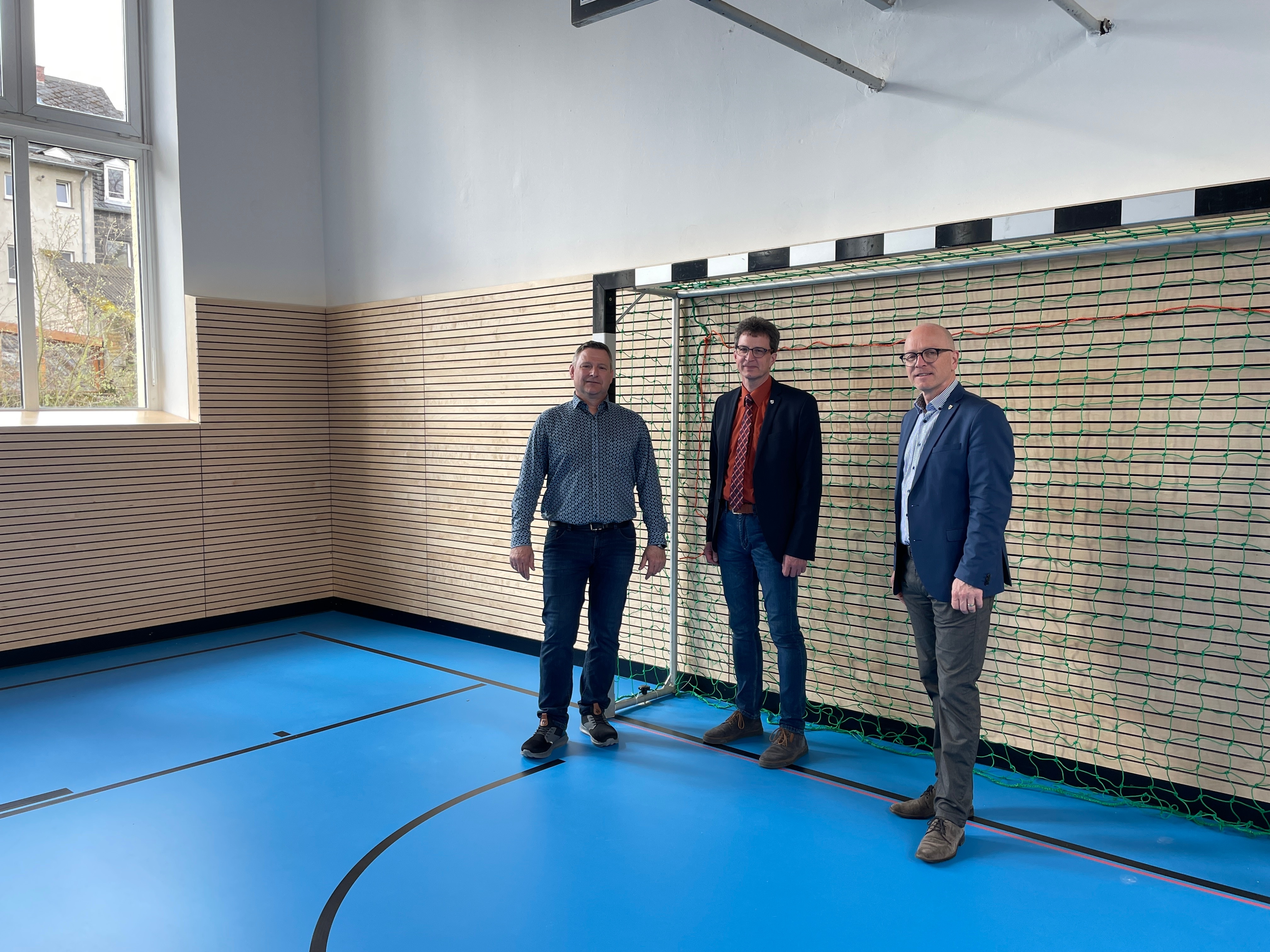 3 Personen stehen in einer Sporthalle vor einem Tor