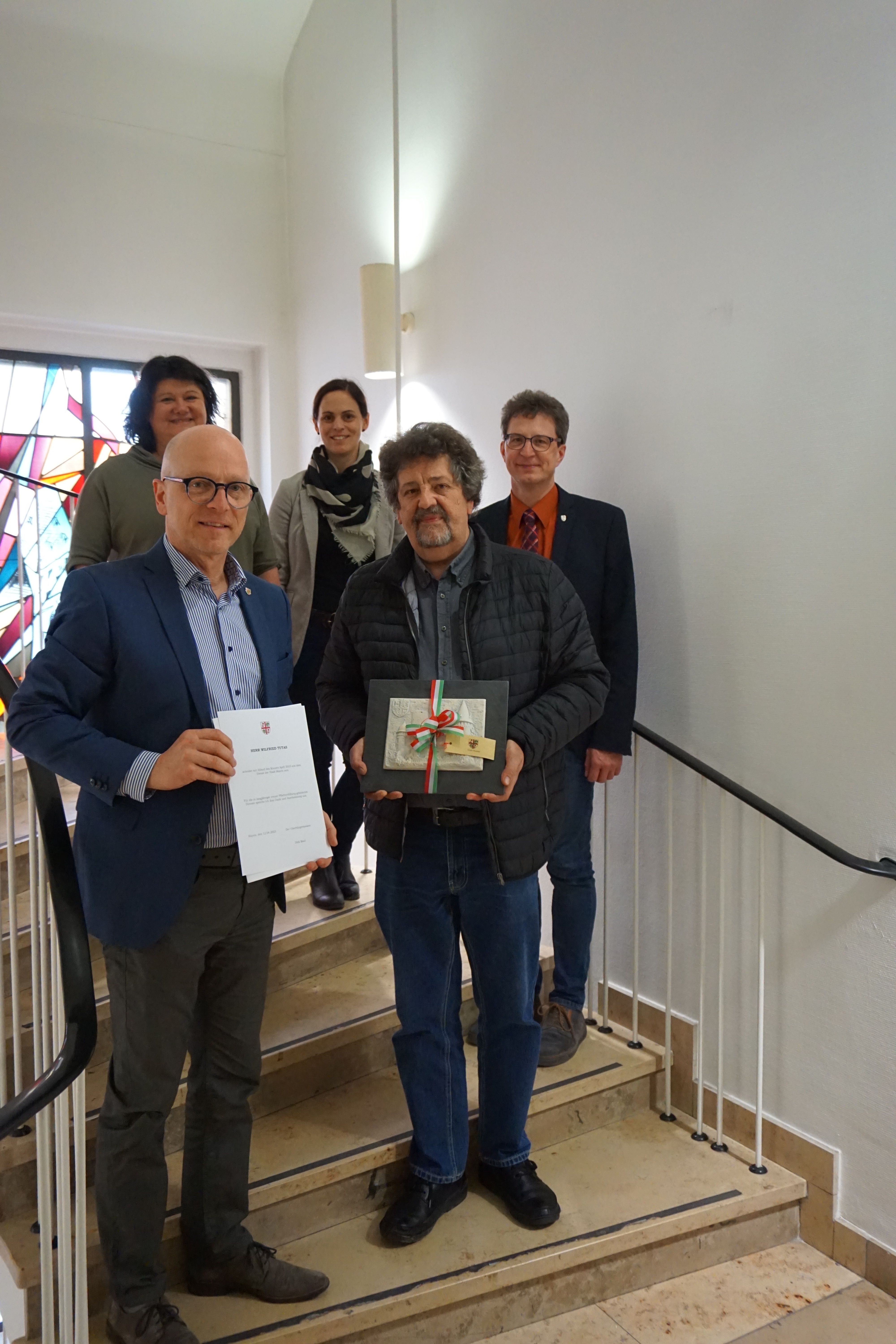 5 Personen stehen auf einer Treppe - einer hält ein Präsent, ein anderer eine Urkunde in den Händen