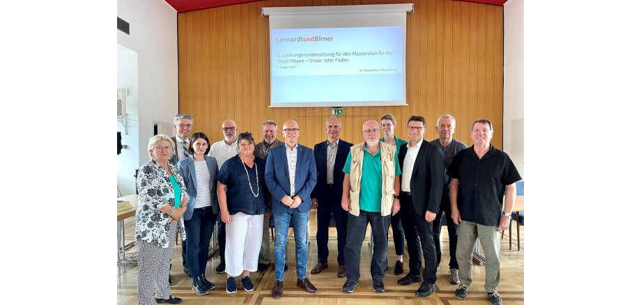 Die Mitglieder der Lenkungsrunde zusammen mit dem Vorsitzenden Oberbürgermeister Dirk Meid Eine Gruppe steht im Sitzungssaal zur Lenkungsrunde versammelt