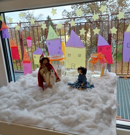 Zwei Figuren und 2 Teelichter vor einem geschmückten Fenster