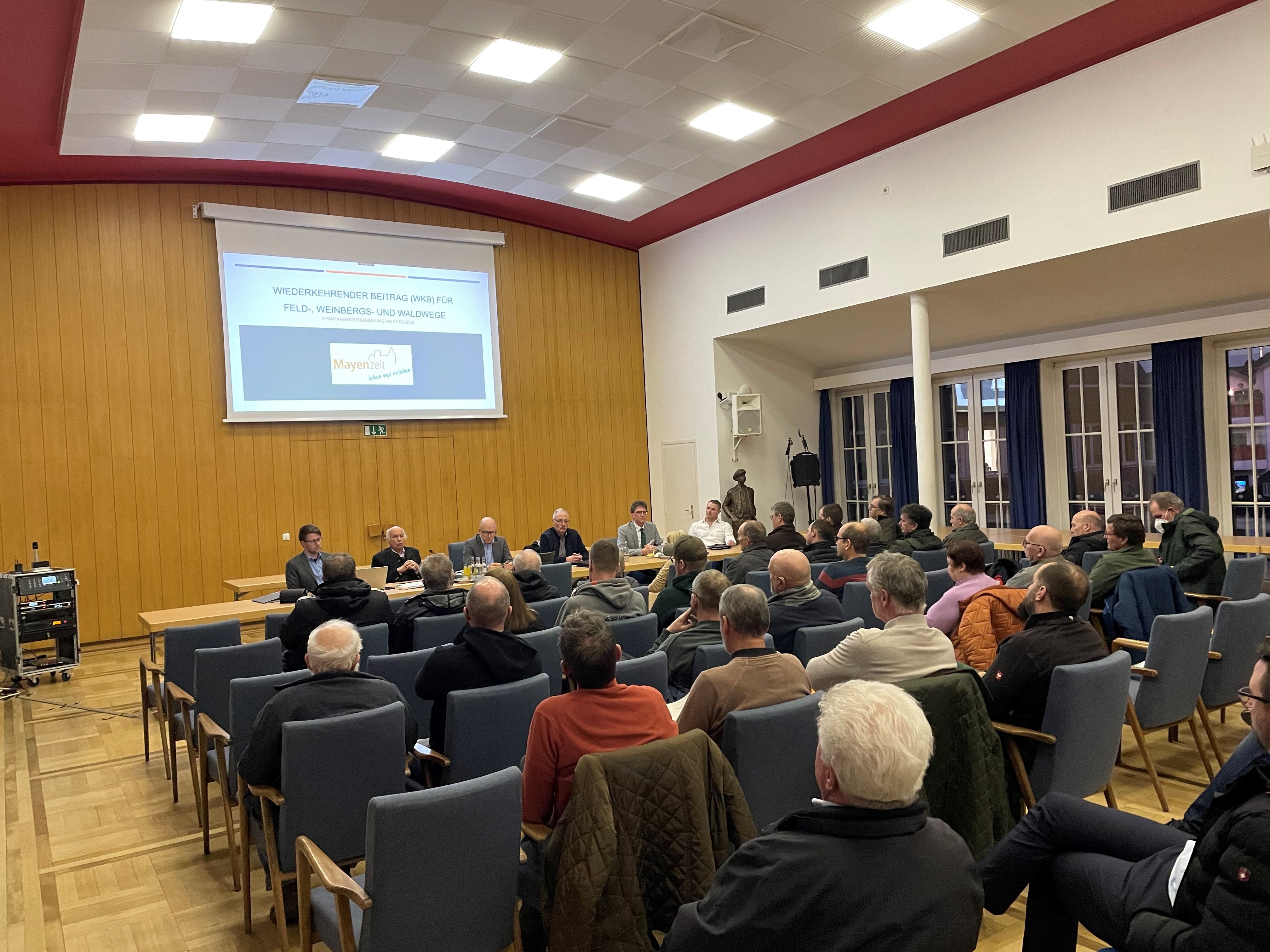 Im Sitzungssaal des Rathauses hören die Bürger zu und schauen auf einen Bildschirm mit einer Power Point Präsentation 