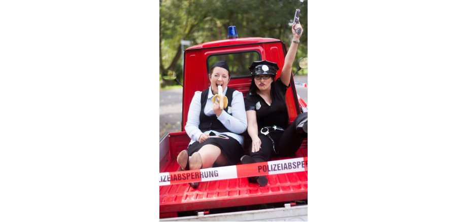 Zwei Frauen im Polizeikostüm auf der Ladefläche eines roten Fahrzeuges