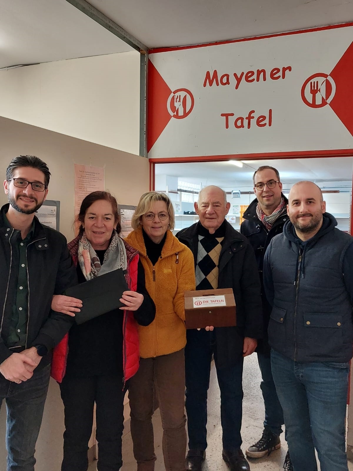 6 Personen stehen in einem Durchgang von der Mayener Tafel