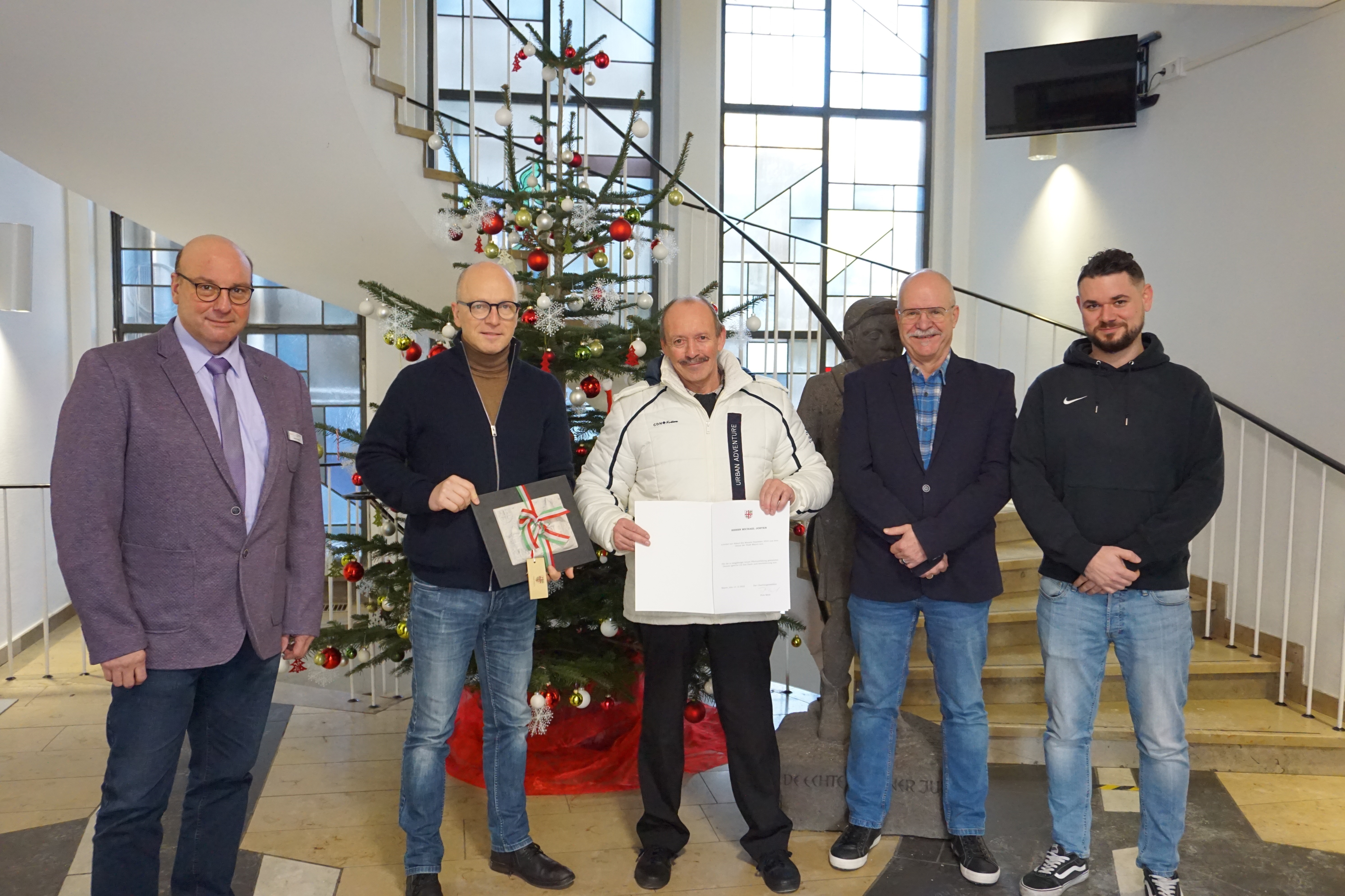 5 Personen stehen zusammen, 2 halten ein Geschenk und eine Urkunde in der Hand