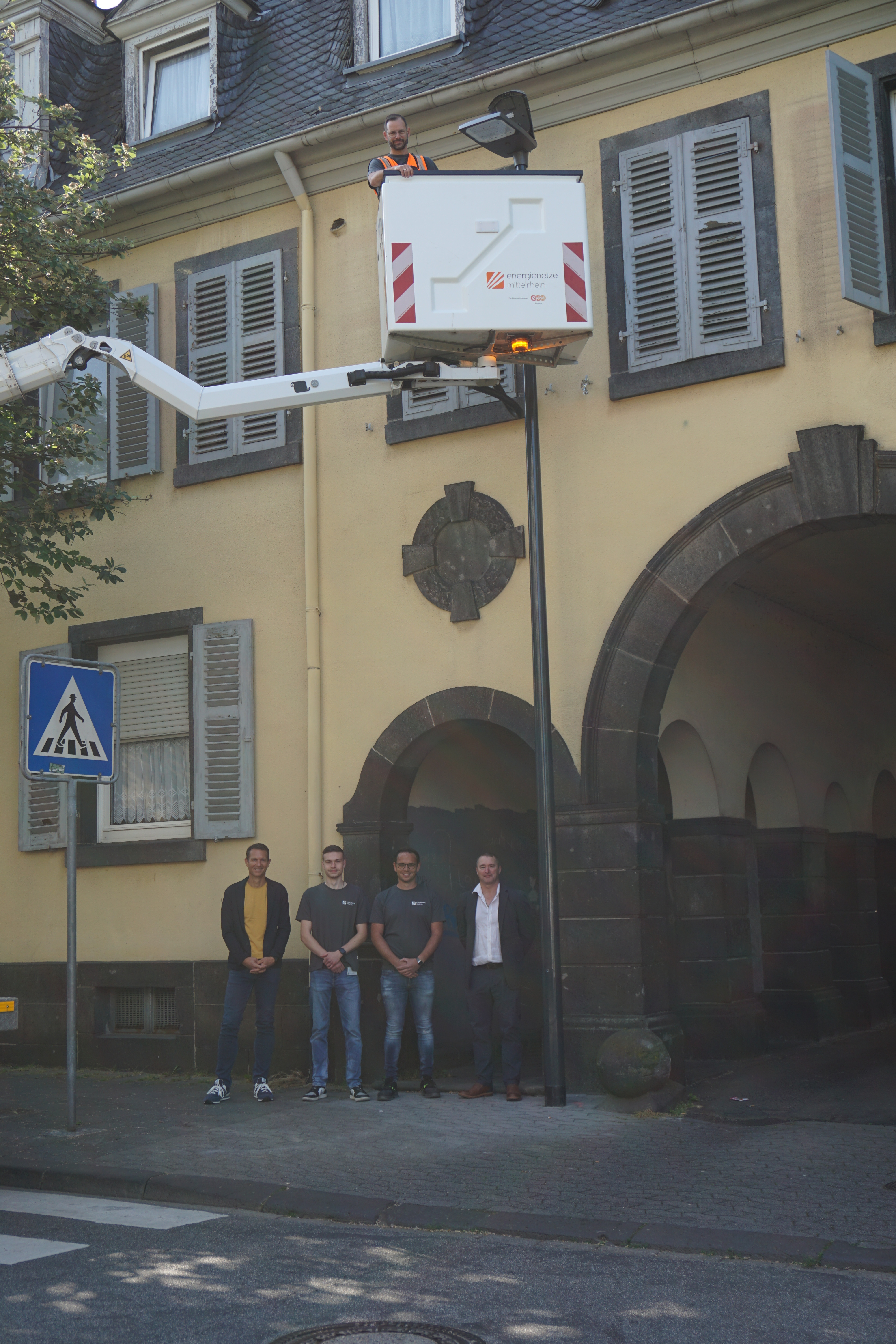 4 Männer stehen zusammen - darüber eine Person in einem Korb von einem Hubwagen an einer Laterne