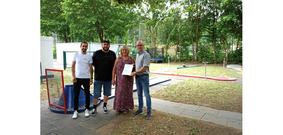 4 Personen vor einem Minigolfplatz - einer hält eine Urkunde in der Hand