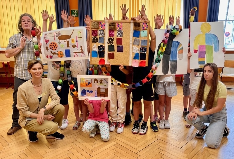 3 Erwachsene und Kinder stehen in einer Gruppe zusammen - die Kinder sind alle durch Plakate verdeckt