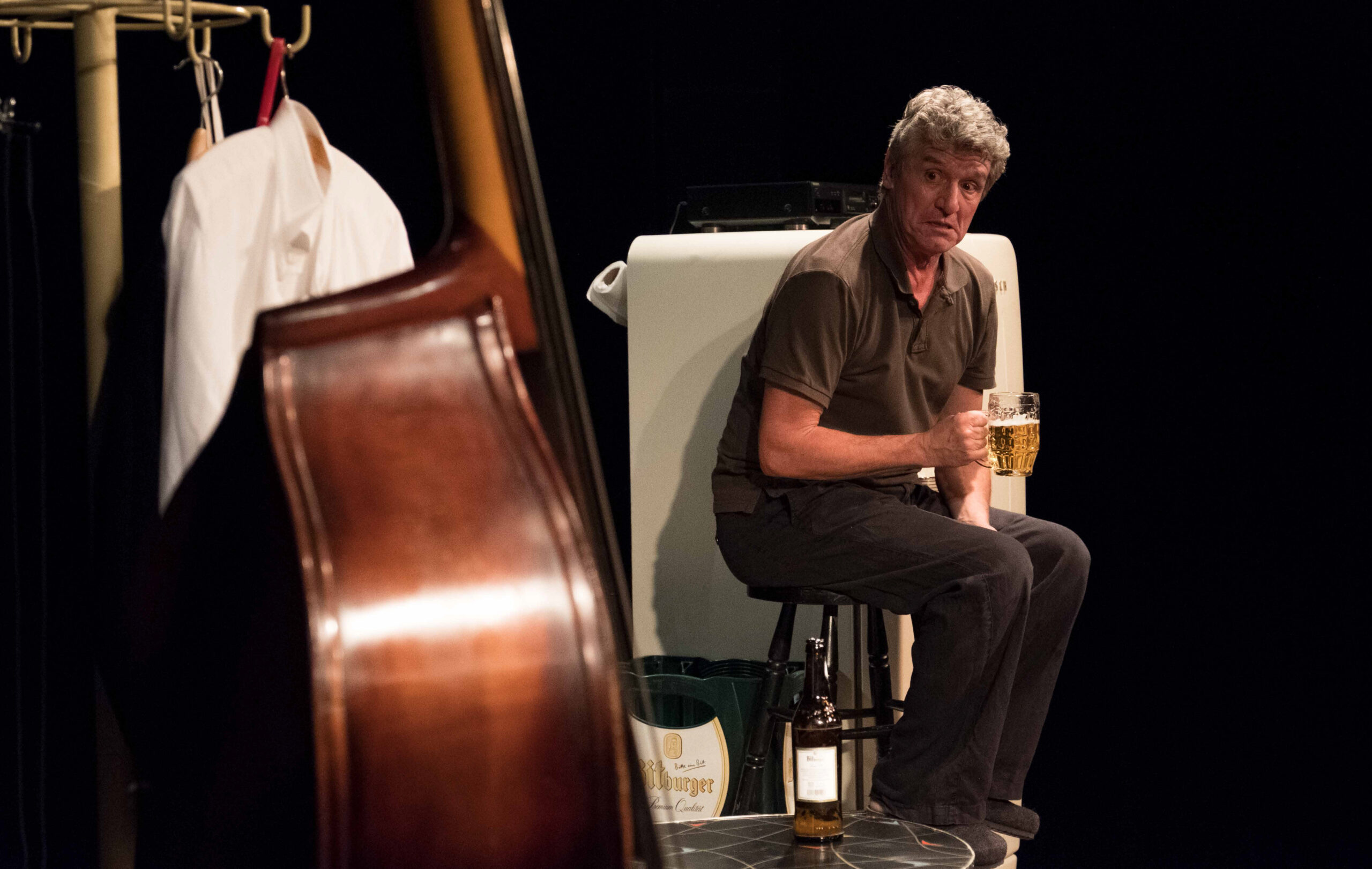 Ein Mann sitzt mit einem Glas Bier auf einem Hocker und schaut auf einen Kontrabass