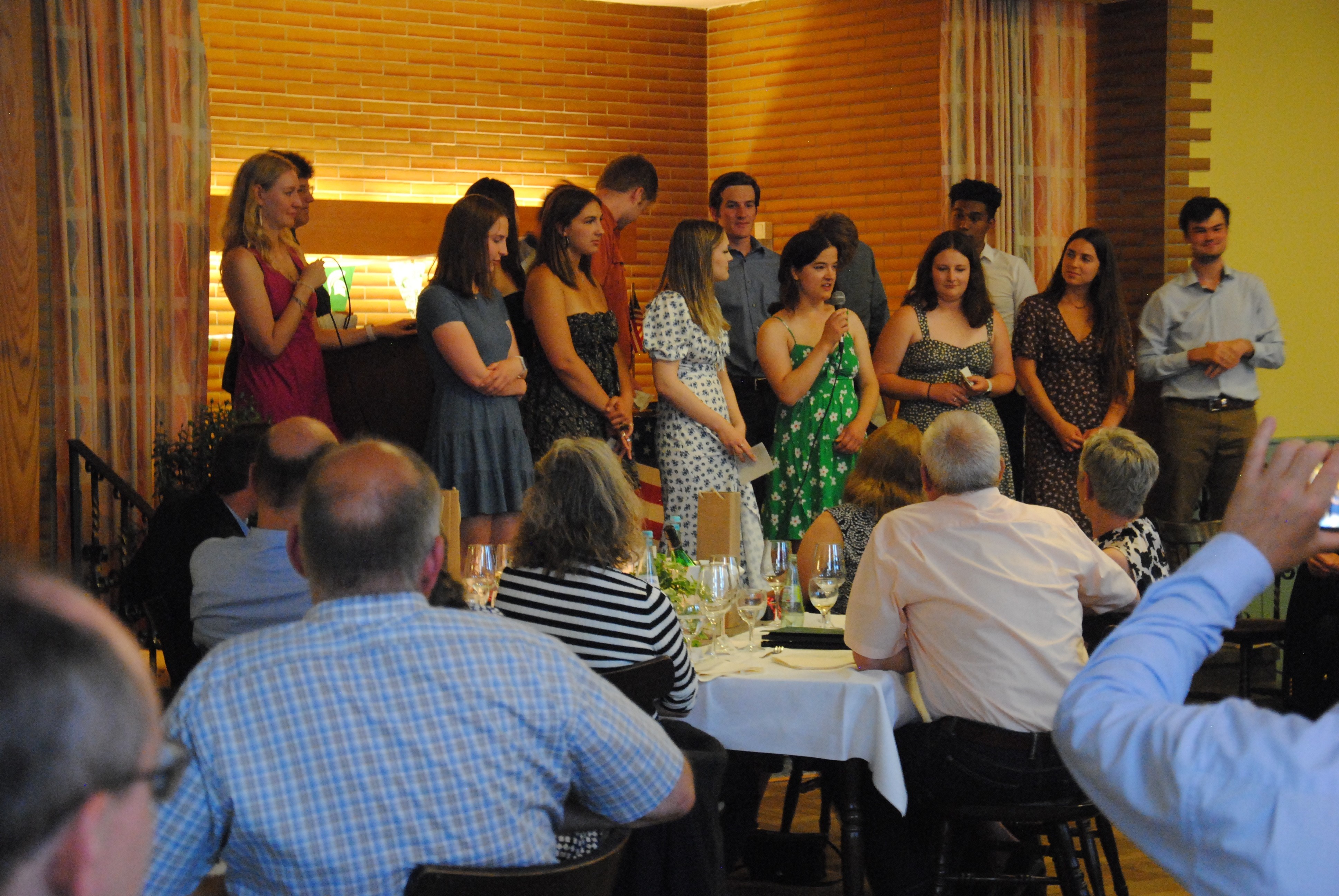 Personen auf einer Bühne und Personen an Tischen, die auf die Bühne schauen