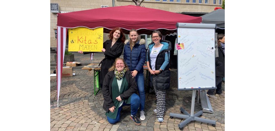 4 Frauen vor einem Pavillon mit Plakaten 