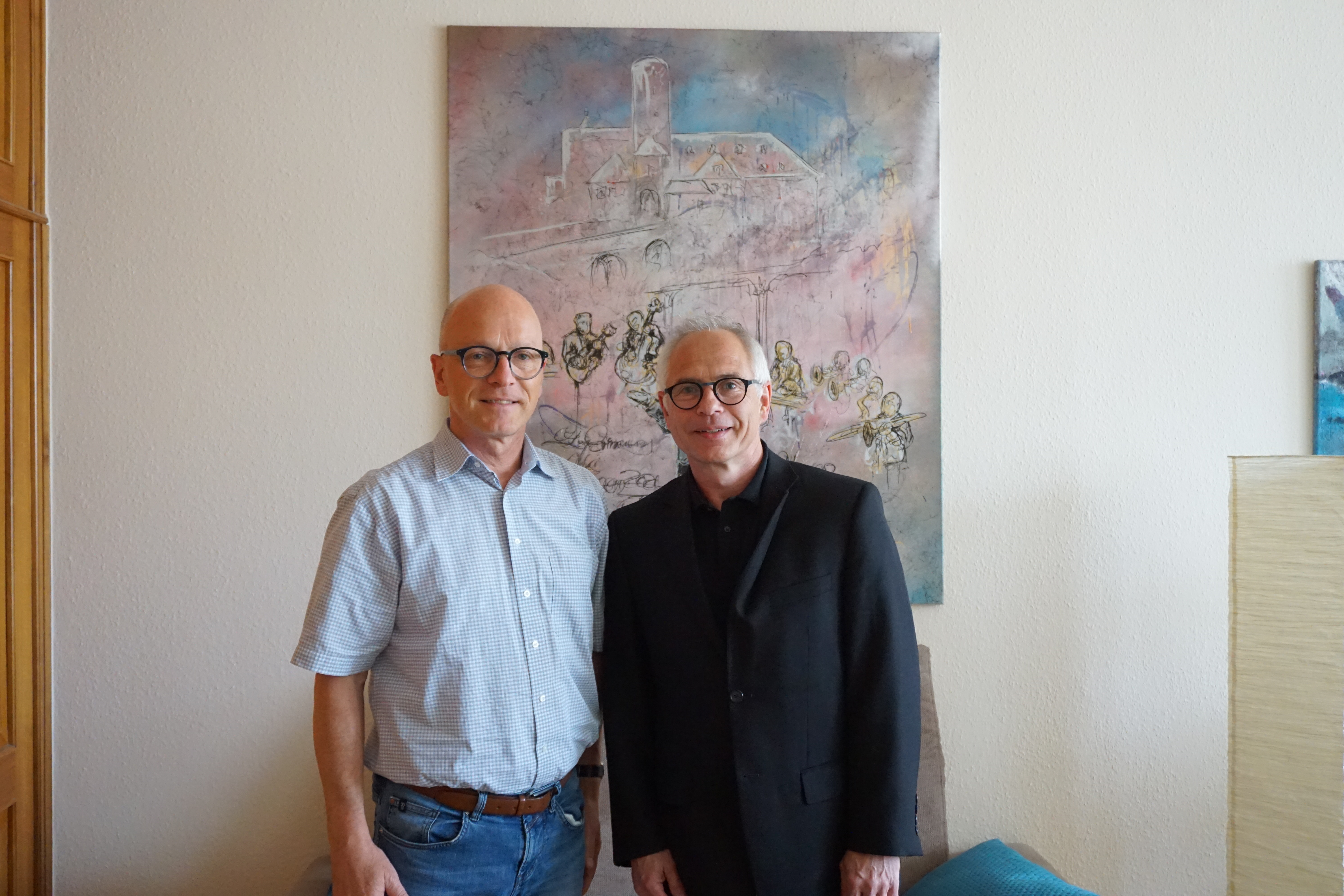 Zwei Personen stehen für ein Bild zusammen - im Hintergrund hängt ein Bild