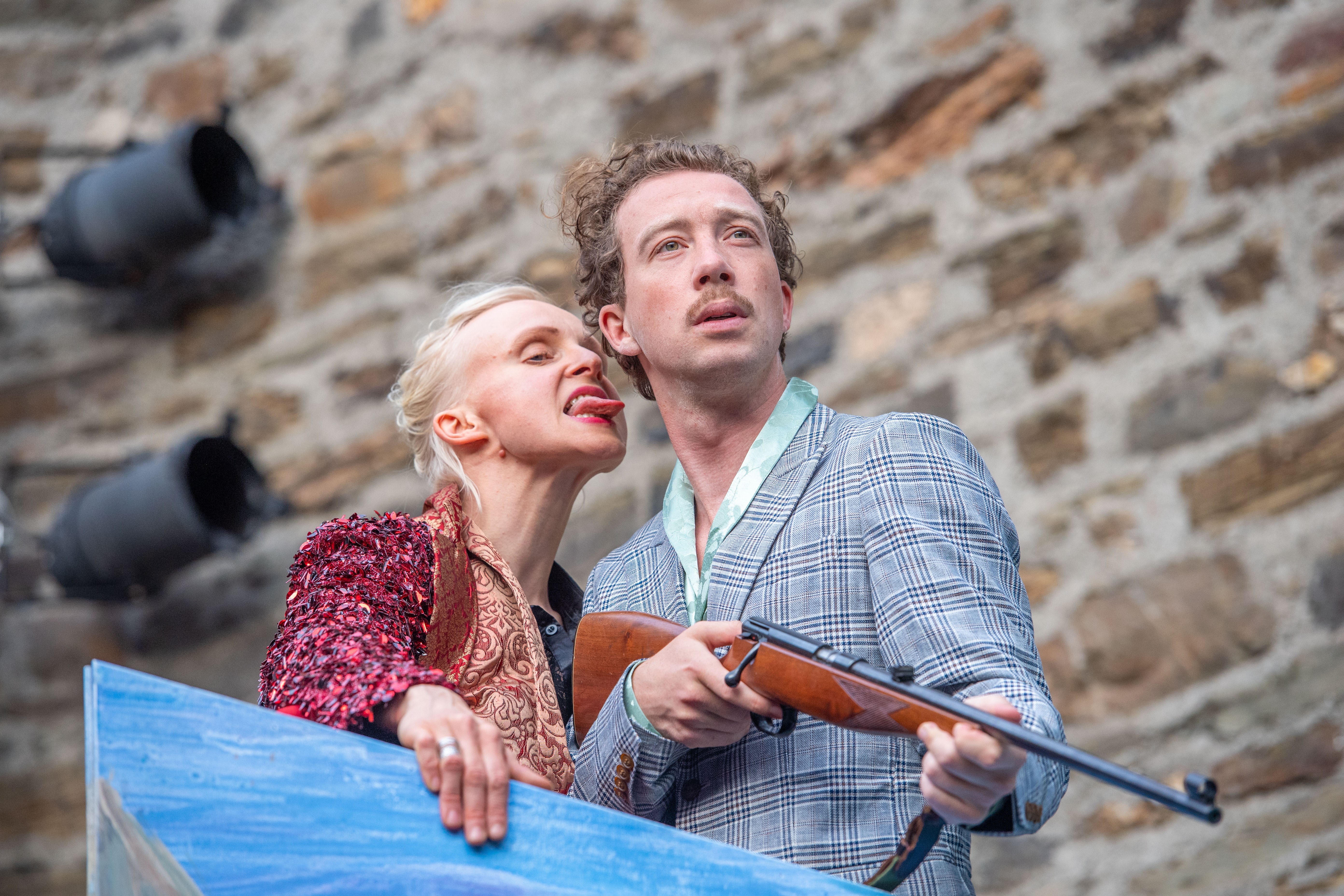 Mann und Frau - Frau steckt die Zunge raus und der Mann hat ein Gewehr in der Hand