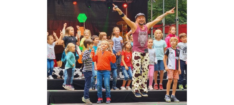 Ein Erwachsener und viele Kinder auf einer Bühne. Es wird gesprungen