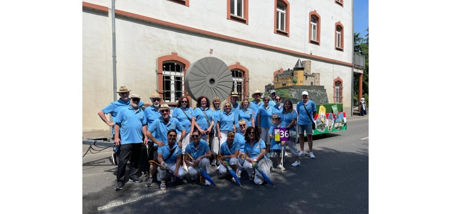 Einheitlich gekleidete Gruppe steht vor einem geschmückten Prunkwagen