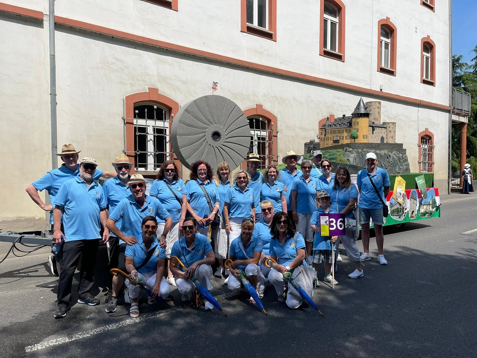 Einheitlich gekleidete Gruppe steht vor einem geschmückten Prunkwagen