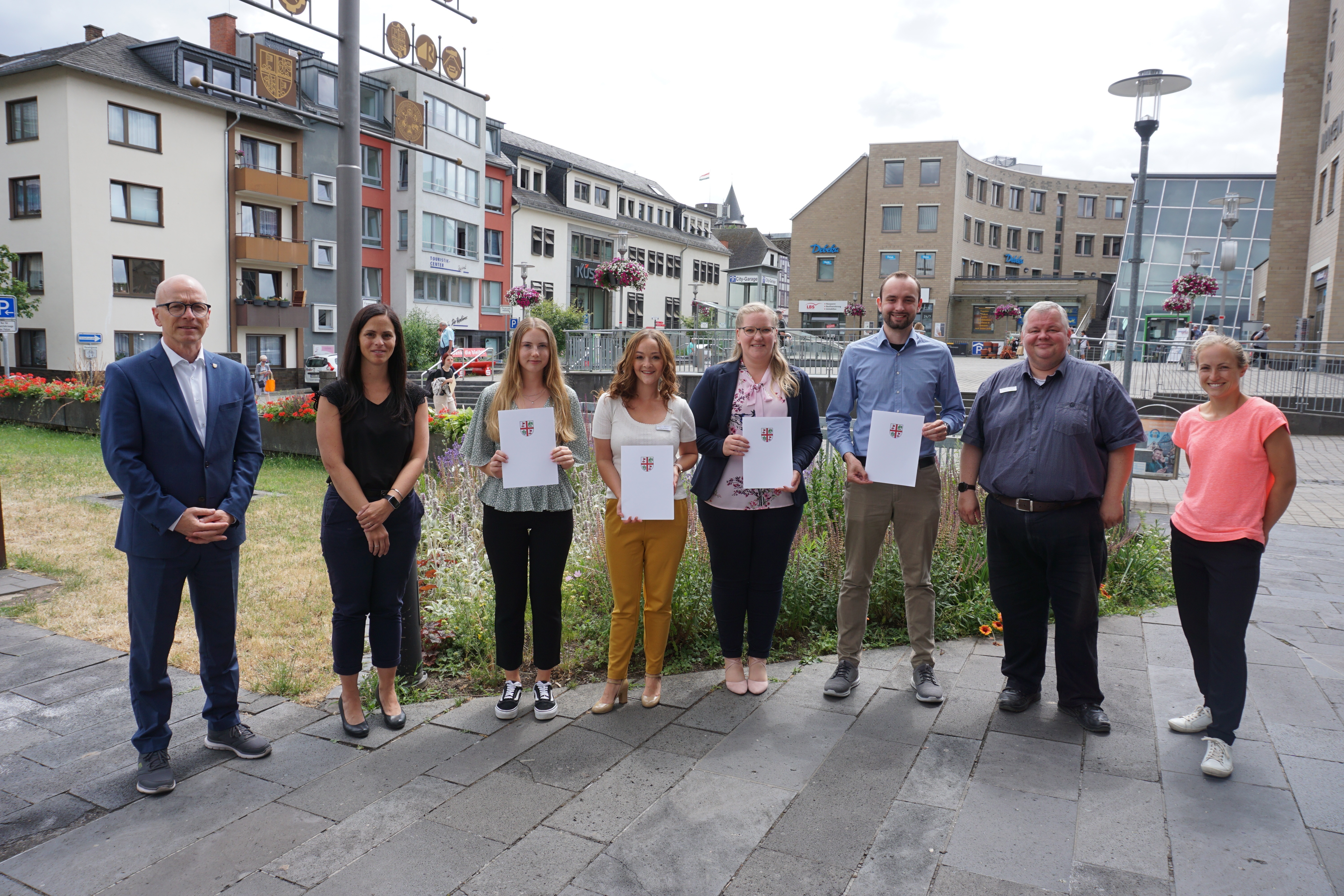 8 Personen stehen vor dem Rathaus zu einem Gruppenbild zusammen - 4 davon halten eine Urkunden in den Händen