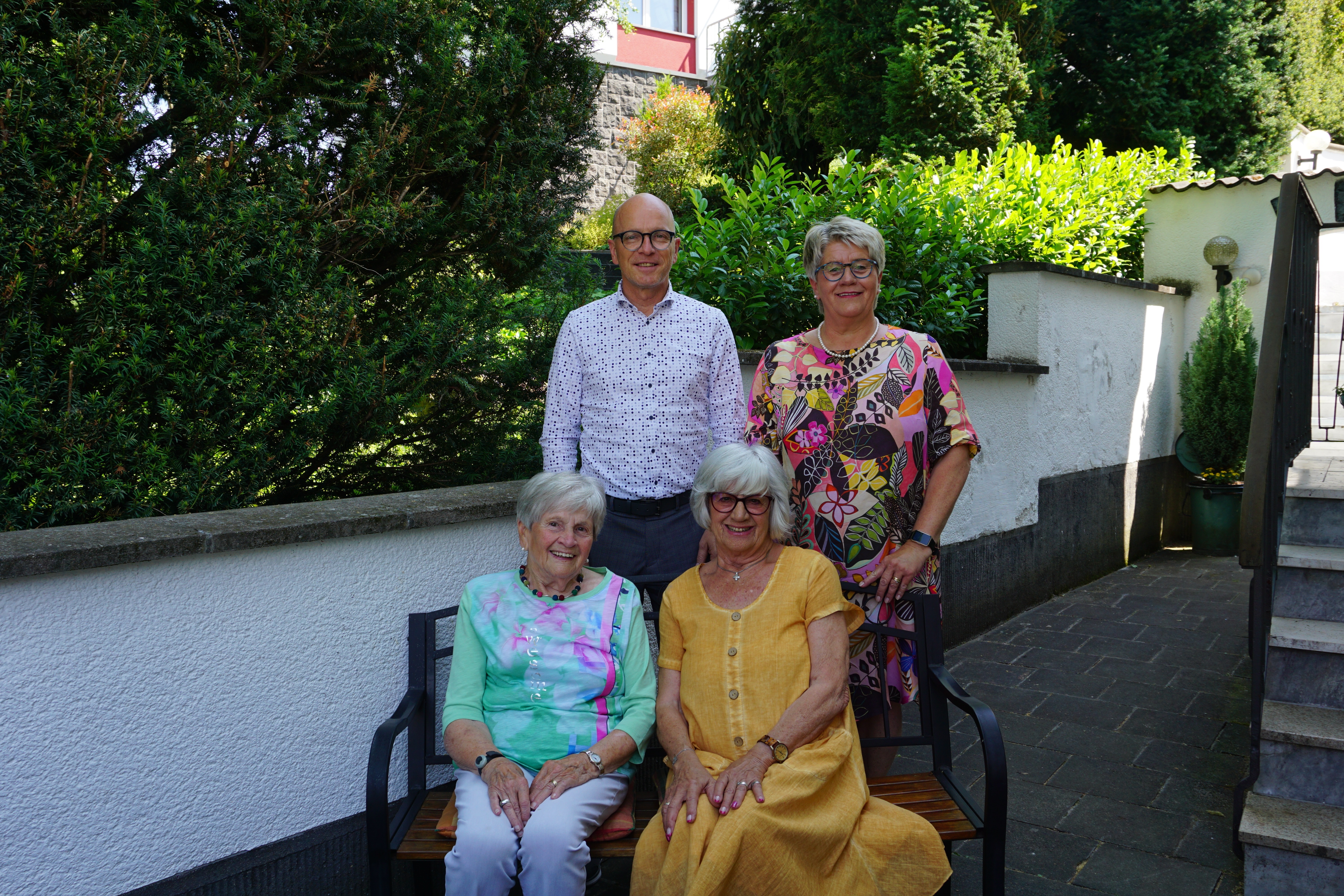 2 Frauen sitzen auf einer Bank, dahinter steht eine Frau und ein Mann für ein Foto