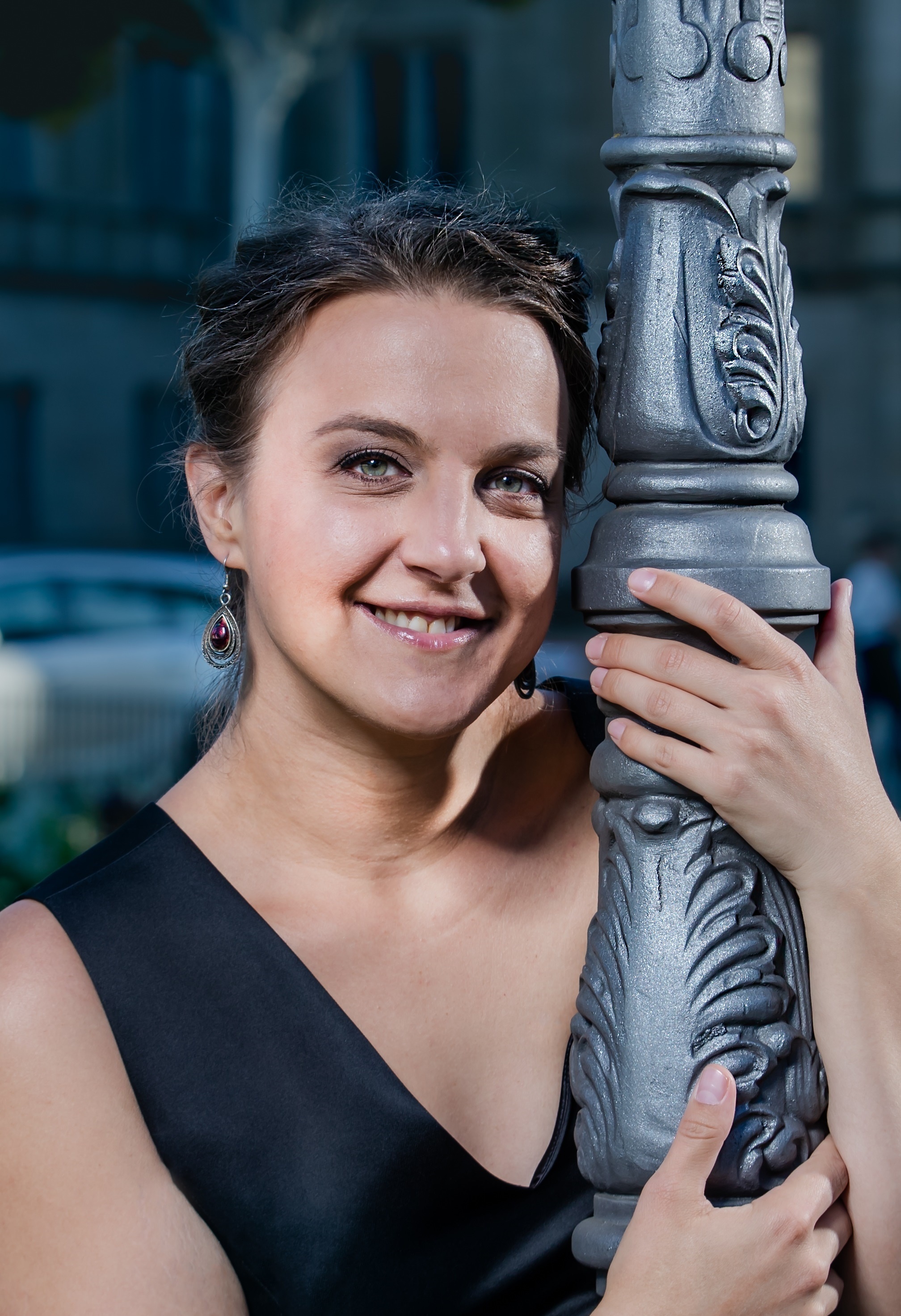 Dunkelhaarige Frau in einem schwarzen Kleid umarmt einen Laternenpfahl 