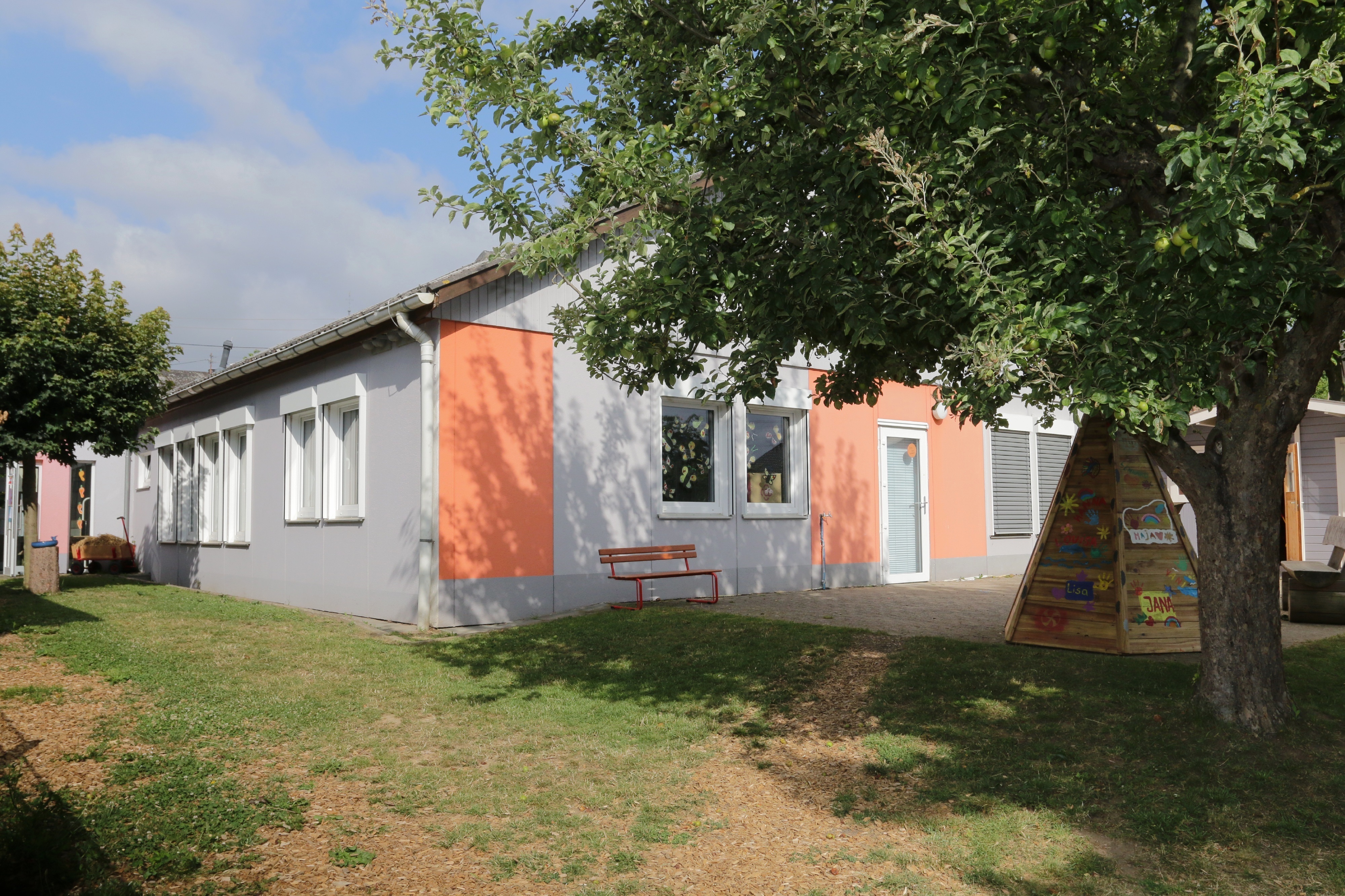 Kindergartengebäude mit Baum und Spielgeräten