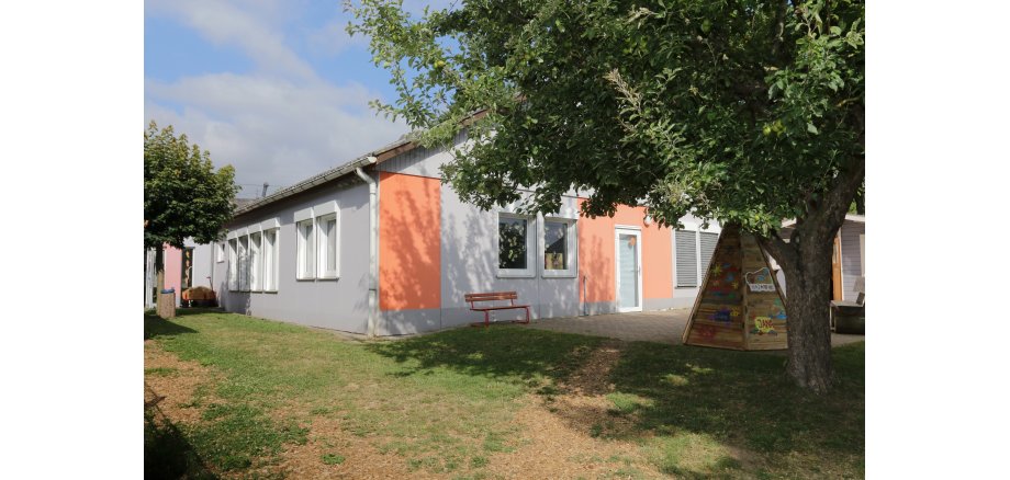 Kindergartengebäude mit Baum und Spielgeräten