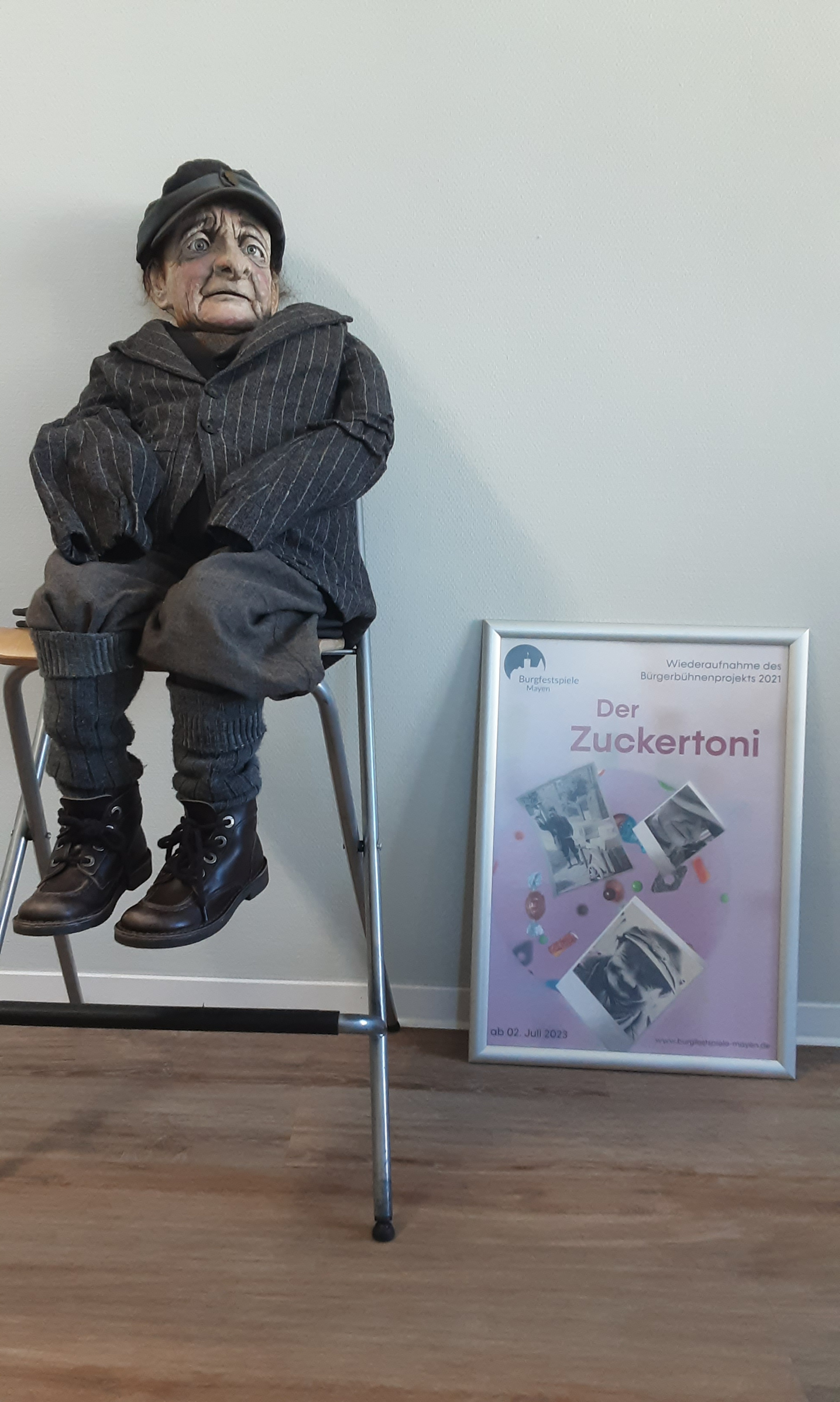 Zuckertoni auf einem Stuhl - daneben das Plakat der Burgfestspiele in einem Bilderrahmen