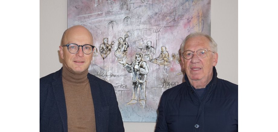 Oberbürgermeister Dirk Meid (links) und Egon Schmitt von der Deutschen Rentenversicherung 2 Personen vor einer Wand mit einem Bild