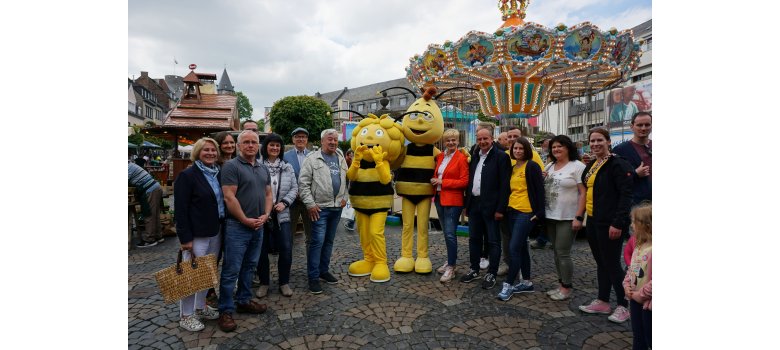 Eine Gruppe von Personen stehen mit der Biene Maya und Willi vor einem Kinderkarussell für ein Bild zusammen