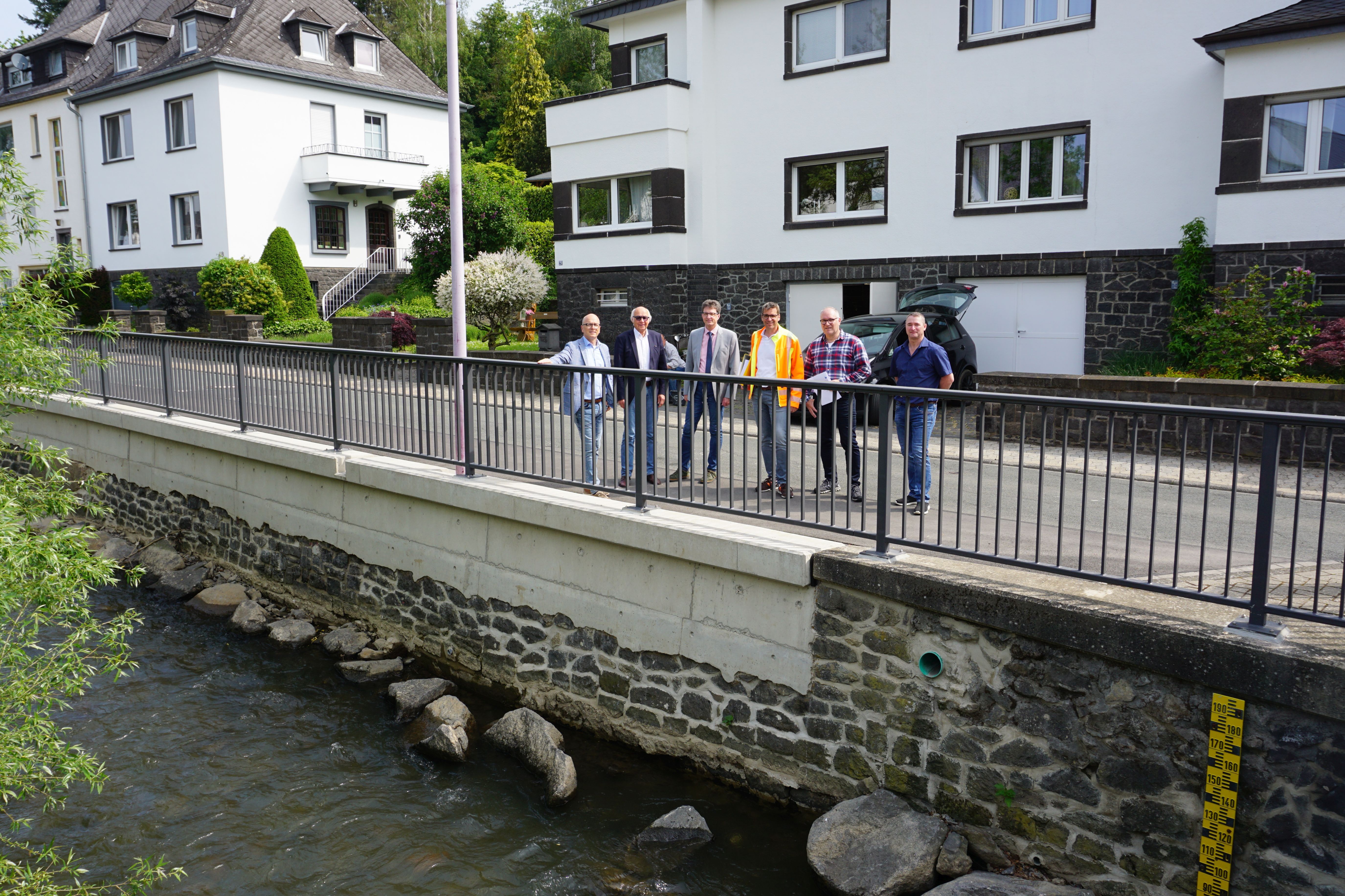 6 Personen stehen auf der Straße an einem Bachlauf