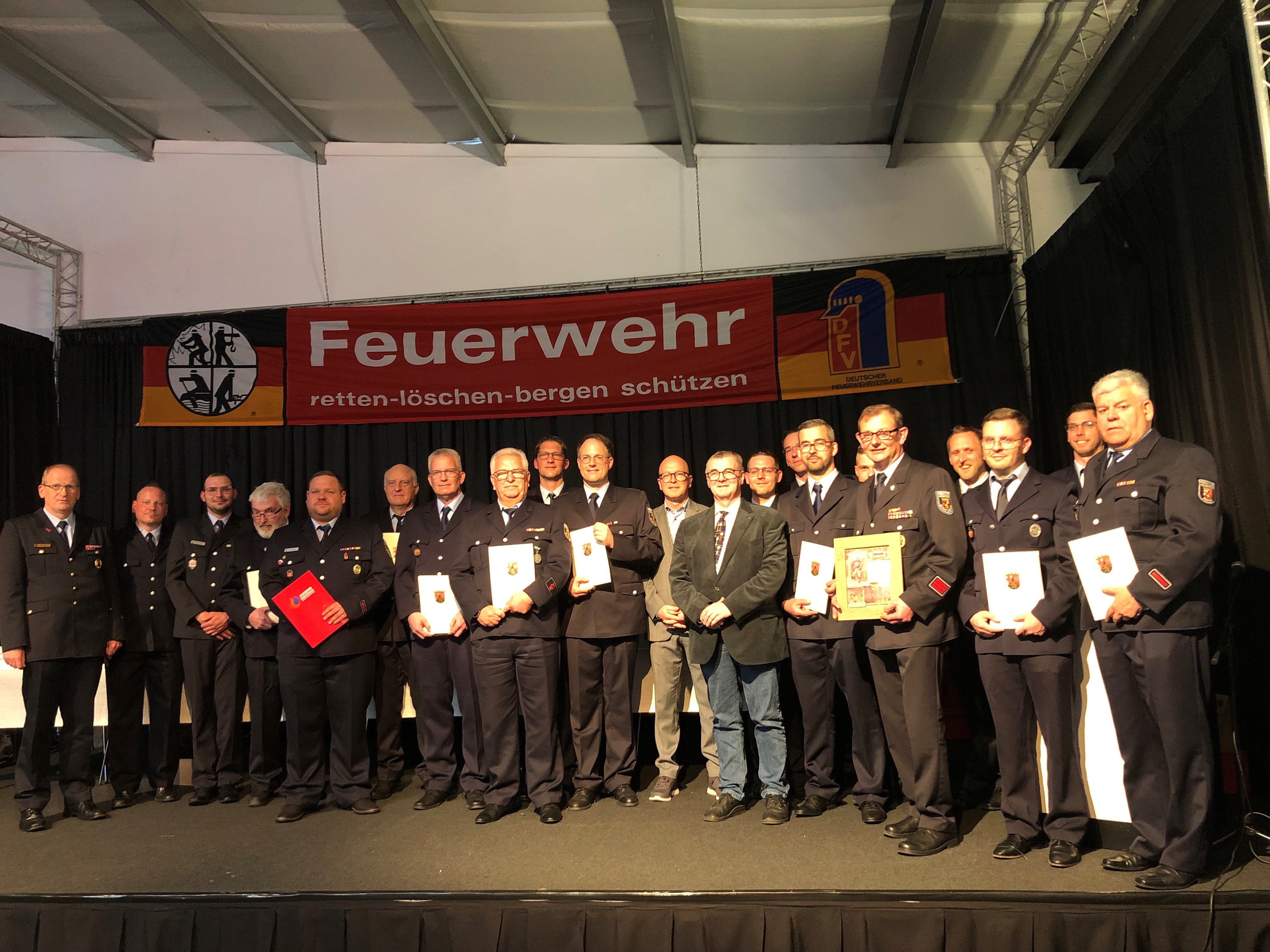 Viele Kameraden und Kameradinnen freuten sich über Ehrungen, Ernennungen, Beförderungen und Verpflichtungen Gruppenbild von Feuerwehrkameradinnen und Kameraden auf einer Bühne und im Anzug