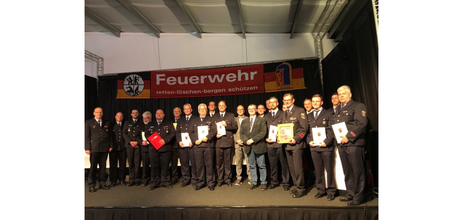 Gruppenbild von Feuerwehrkameradinnen und Kameraden auf einer Bühne und im Anzug