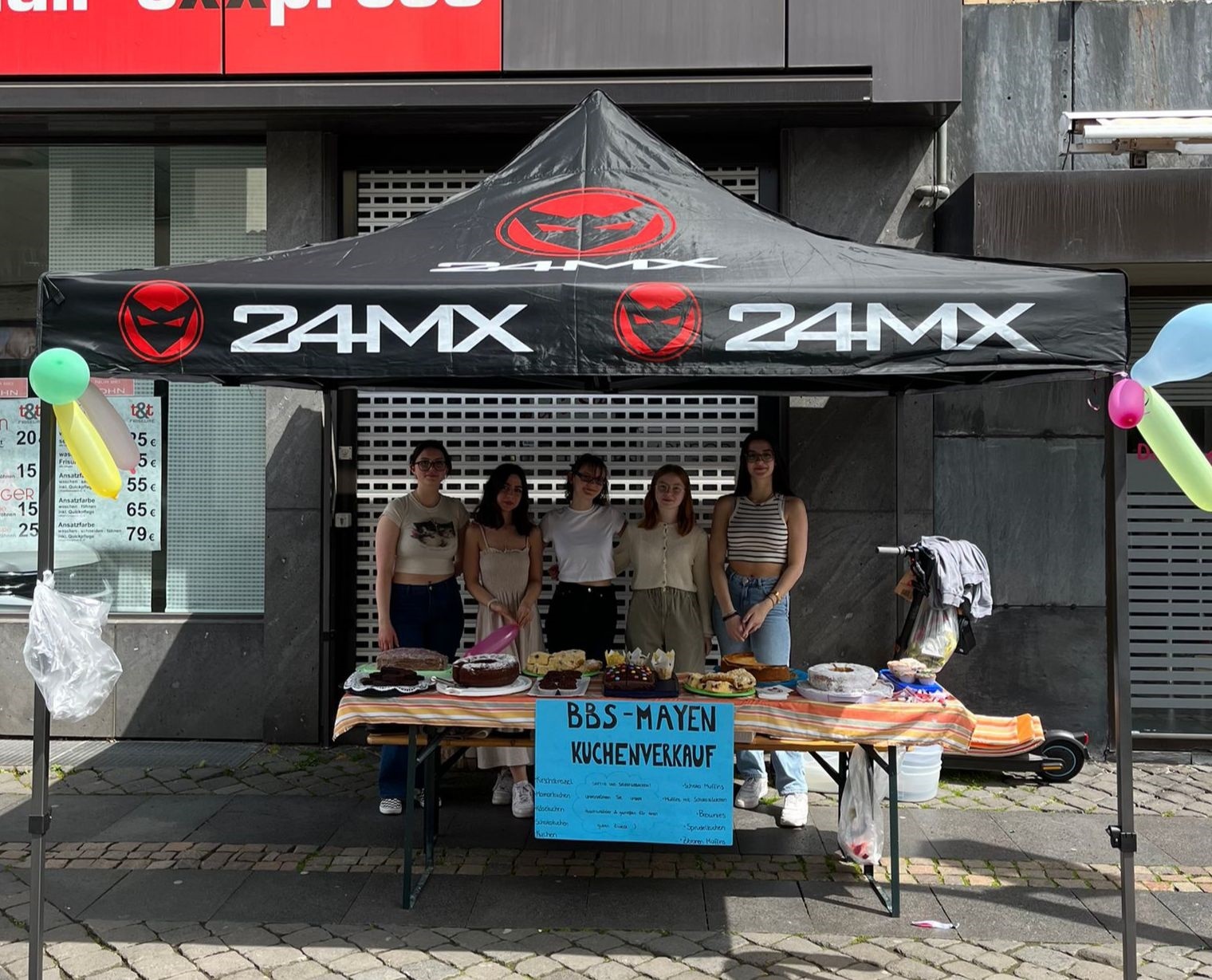 5 Frauen stehen unter einem Pavillon und verkaufen Kuchen