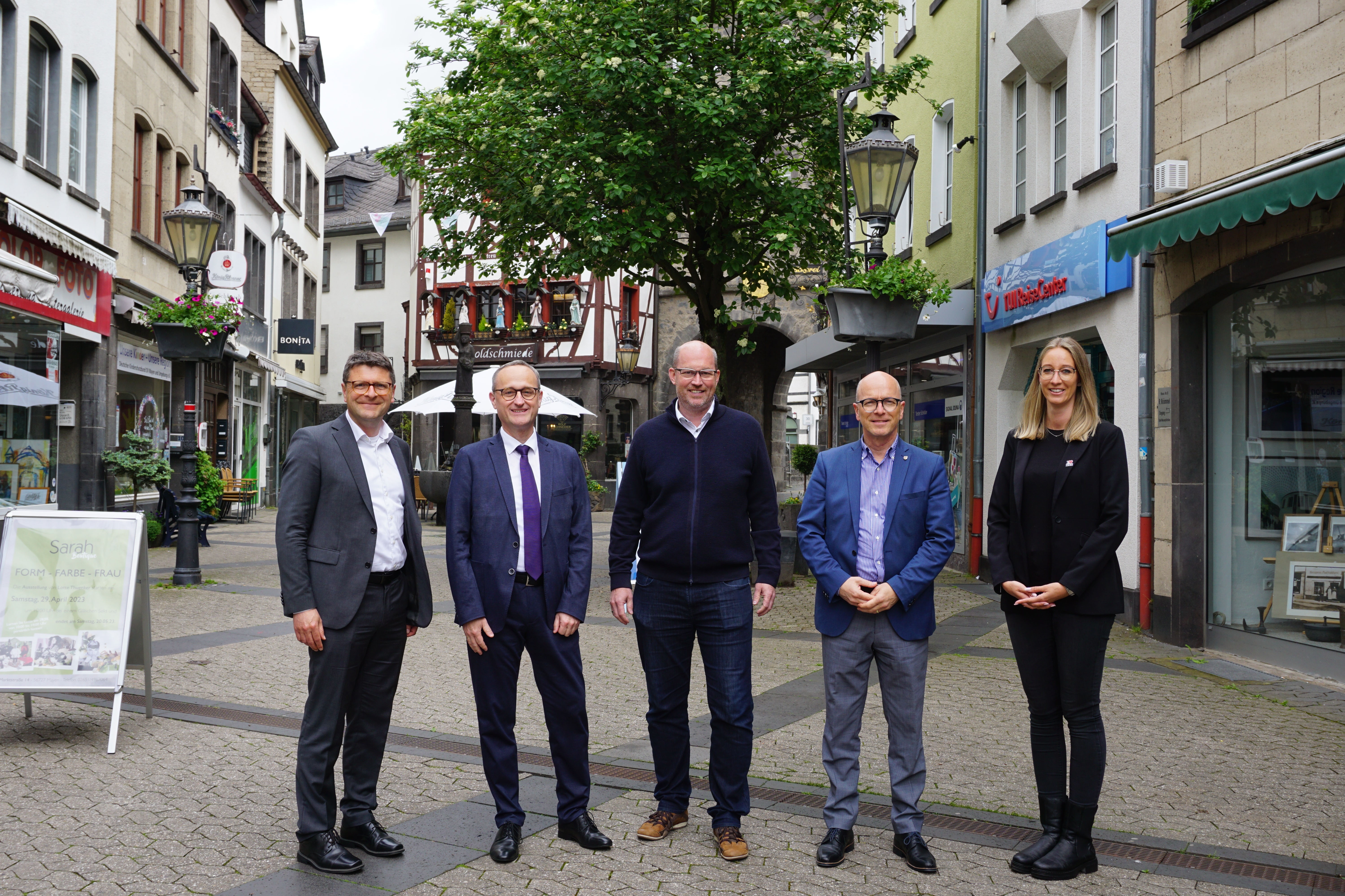 Vier Männer und eine Frau stehen vor einer bepflanzten Blumenampel in der Innenstadt