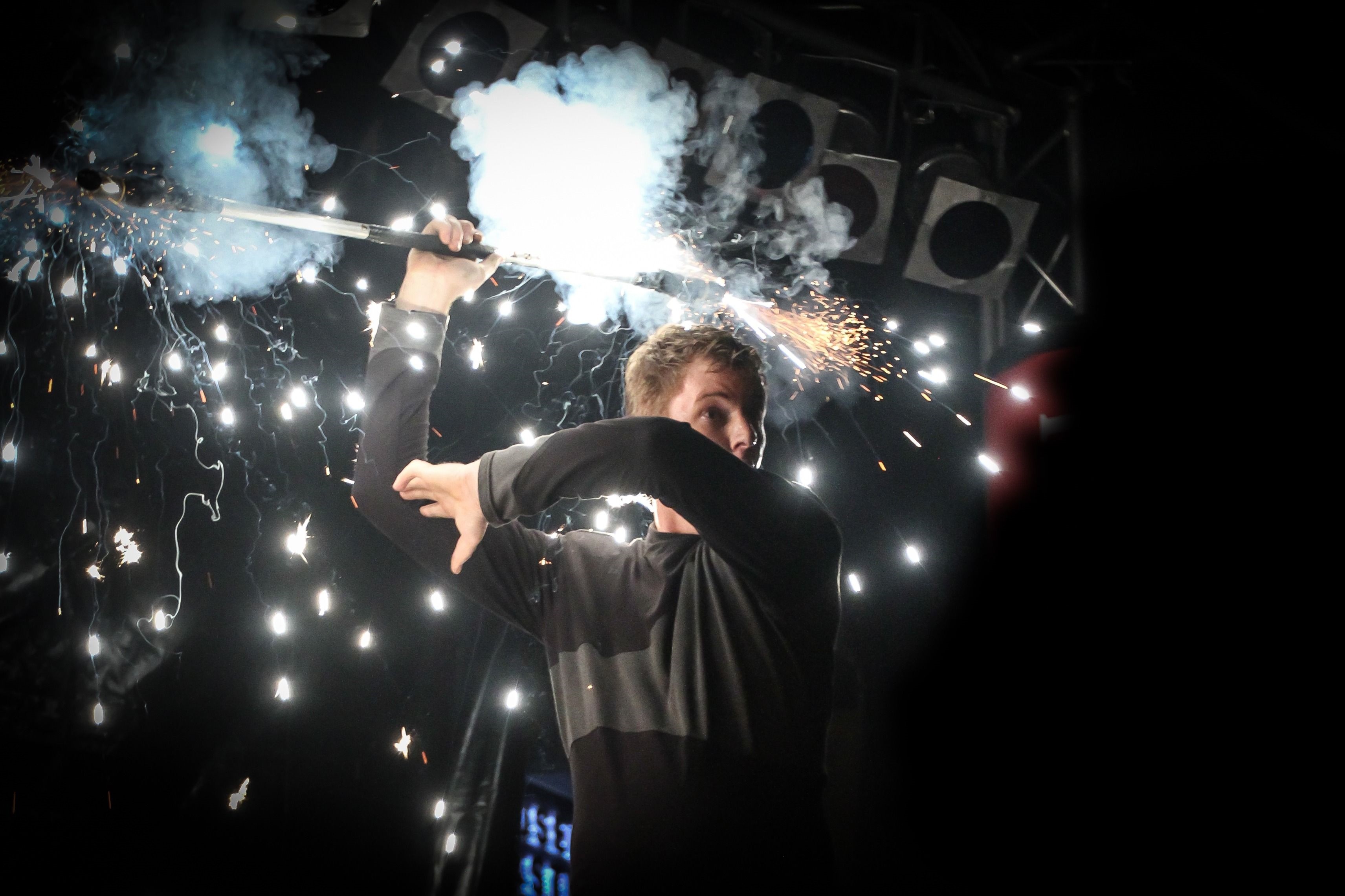 Mann mit Feuerwerk in schwarz gekleidet und vor schwarzem Hintergrund